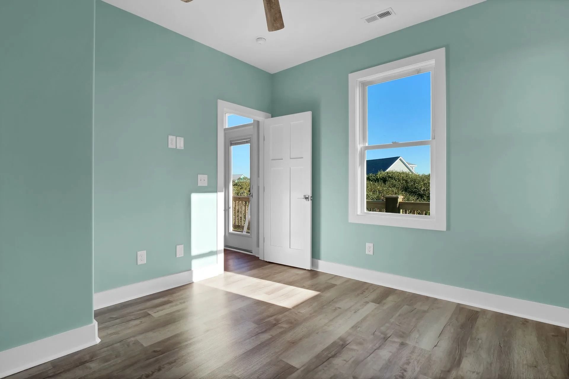 Empty bedroom with blue-green walls, white trim, wood-look flooring, and a door and window.