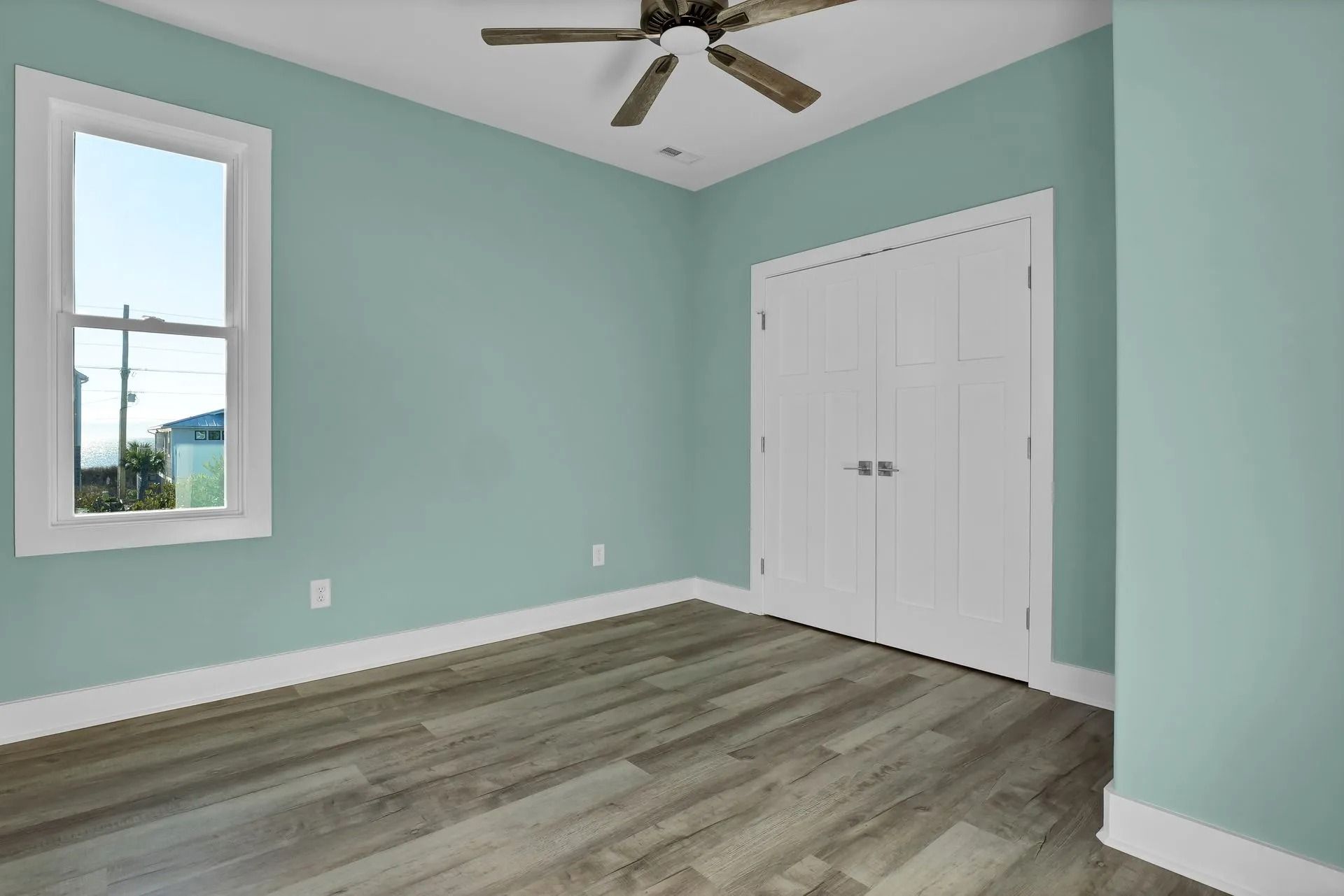 Empty bedroom with light blue walls, white trim, wood-look flooring, a window, and a closed closet.