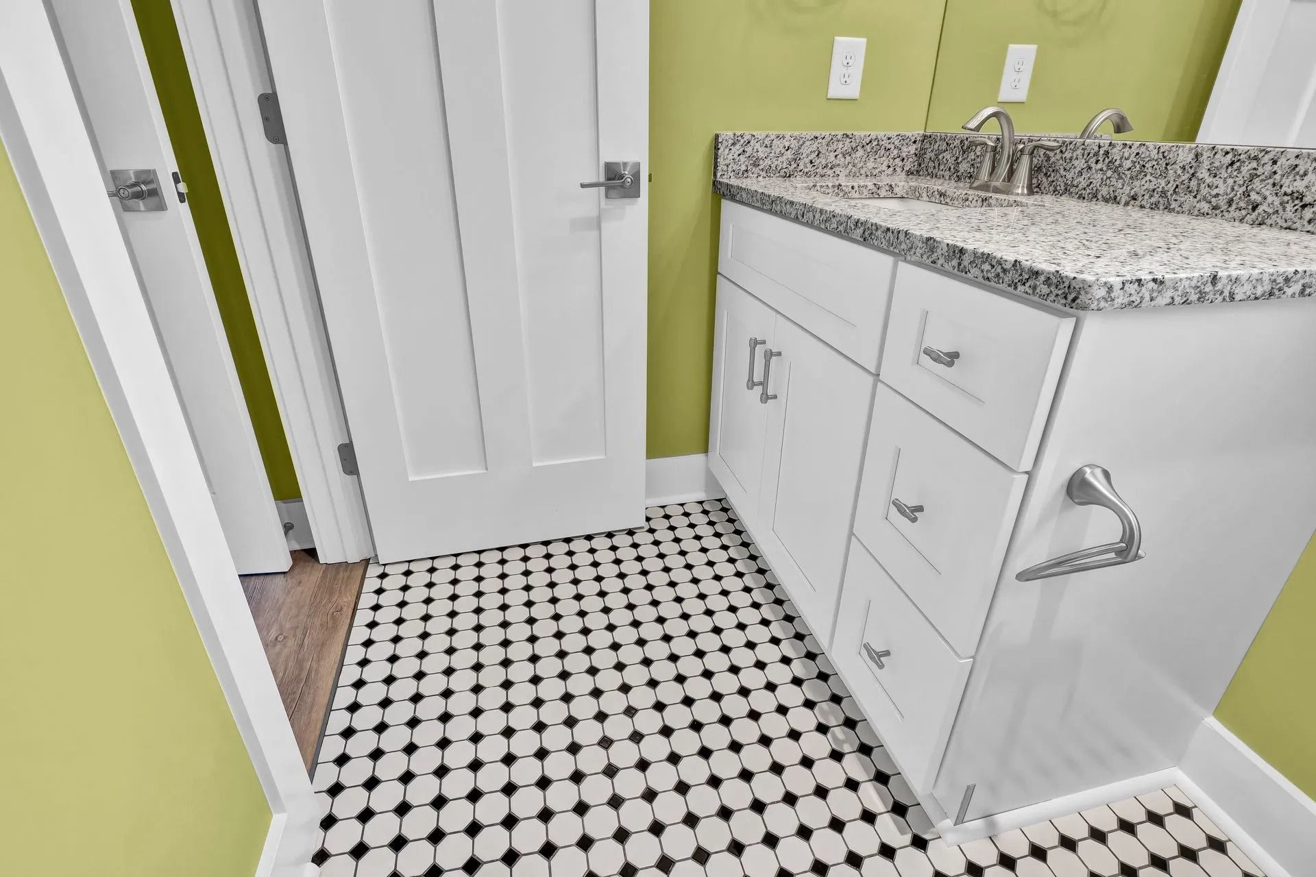 Bathroom with white vanity, granite countertop, black and white tile floor, and a white door.