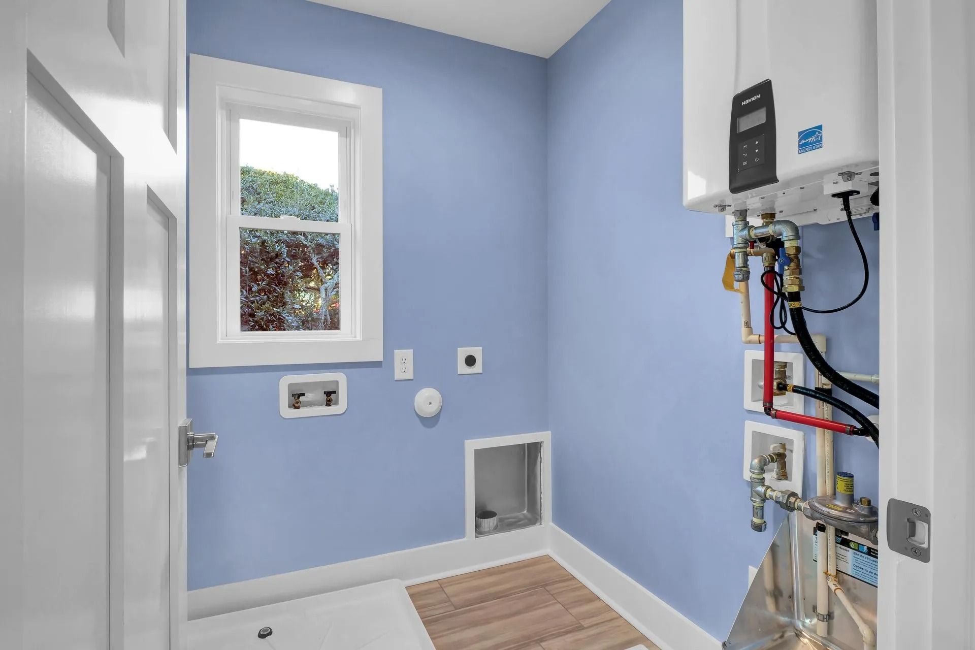 Laundry room with a washing machine hookup, window, and tankless water heater on a light blue wall.