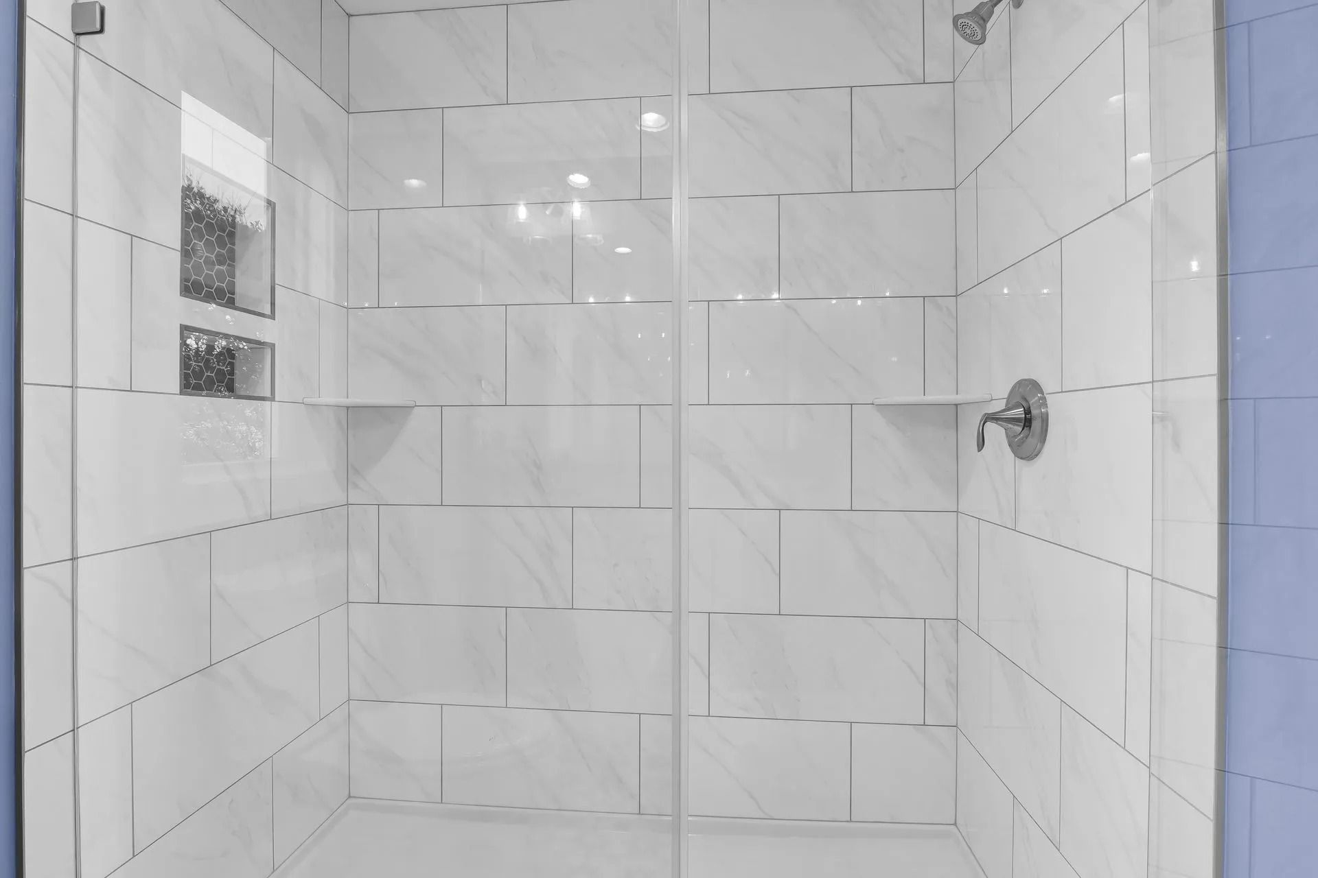 White tiled shower with glass doors and chrome fixtures.