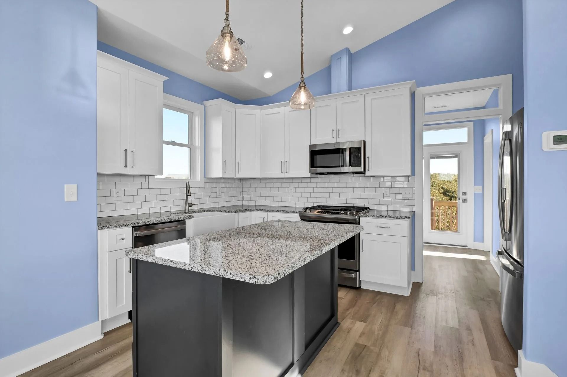 Modern kitchen with white cabinets, gray island, blue walls, and stainless steel appliances.