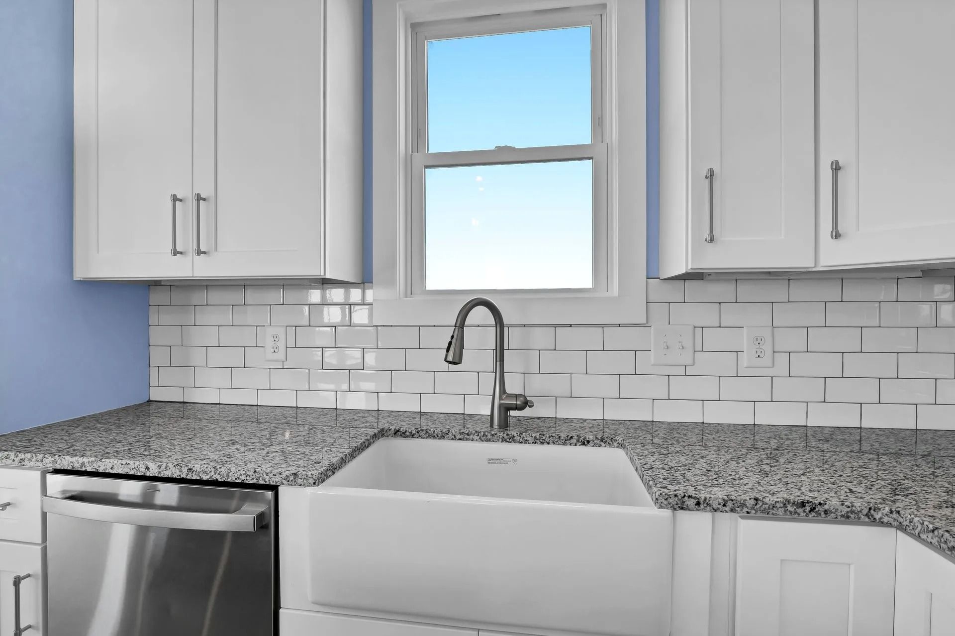 Kitchen with white cabinets, gray countertops, and a white farmhouse sink beneath a window.