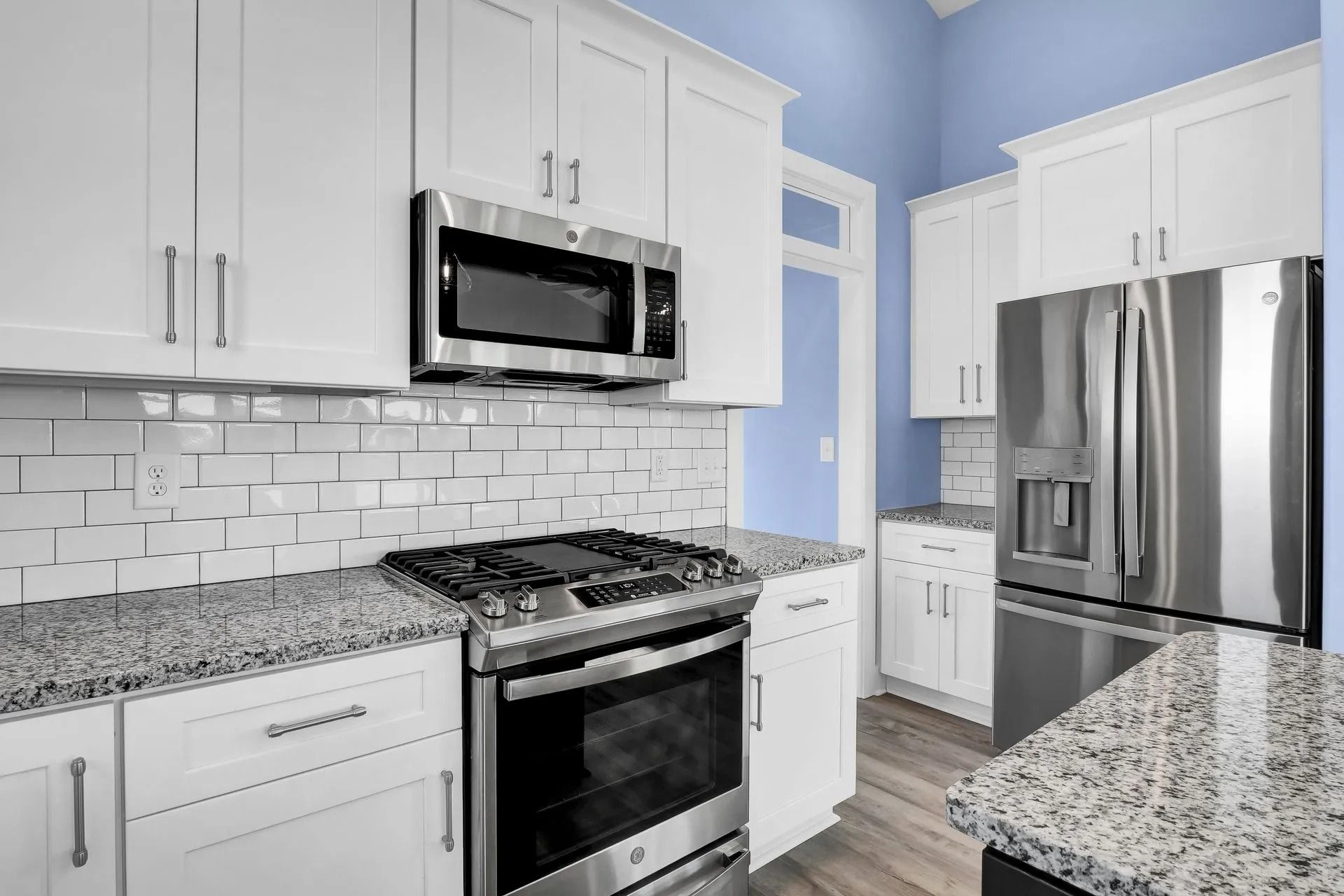 White kitchen with stainless steel appliances, granite countertops, and light blue walls.