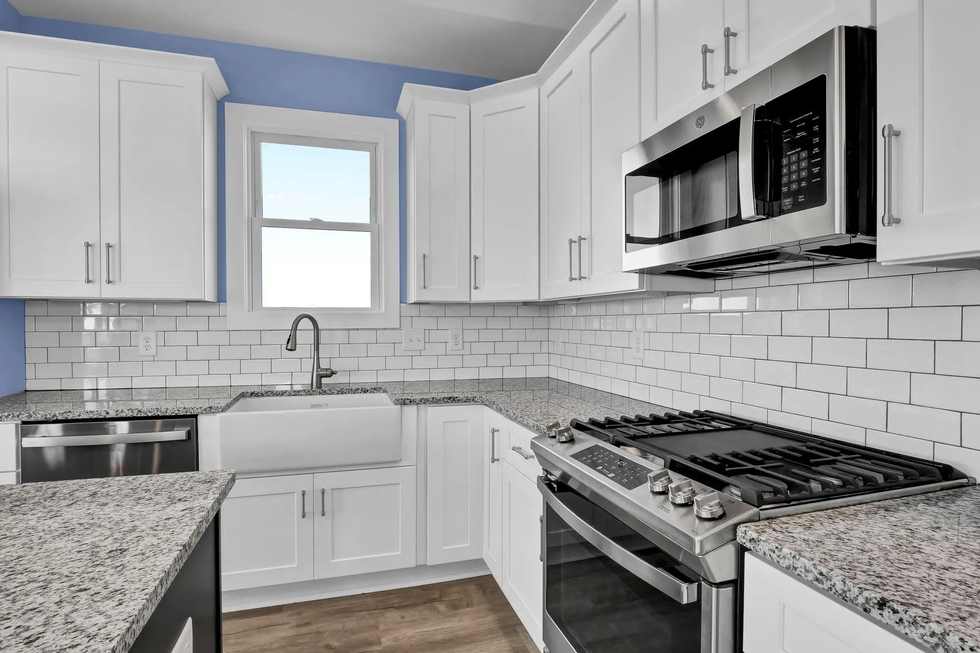 White kitchen with stainless steel appliances, granite countertops, and blue wall.