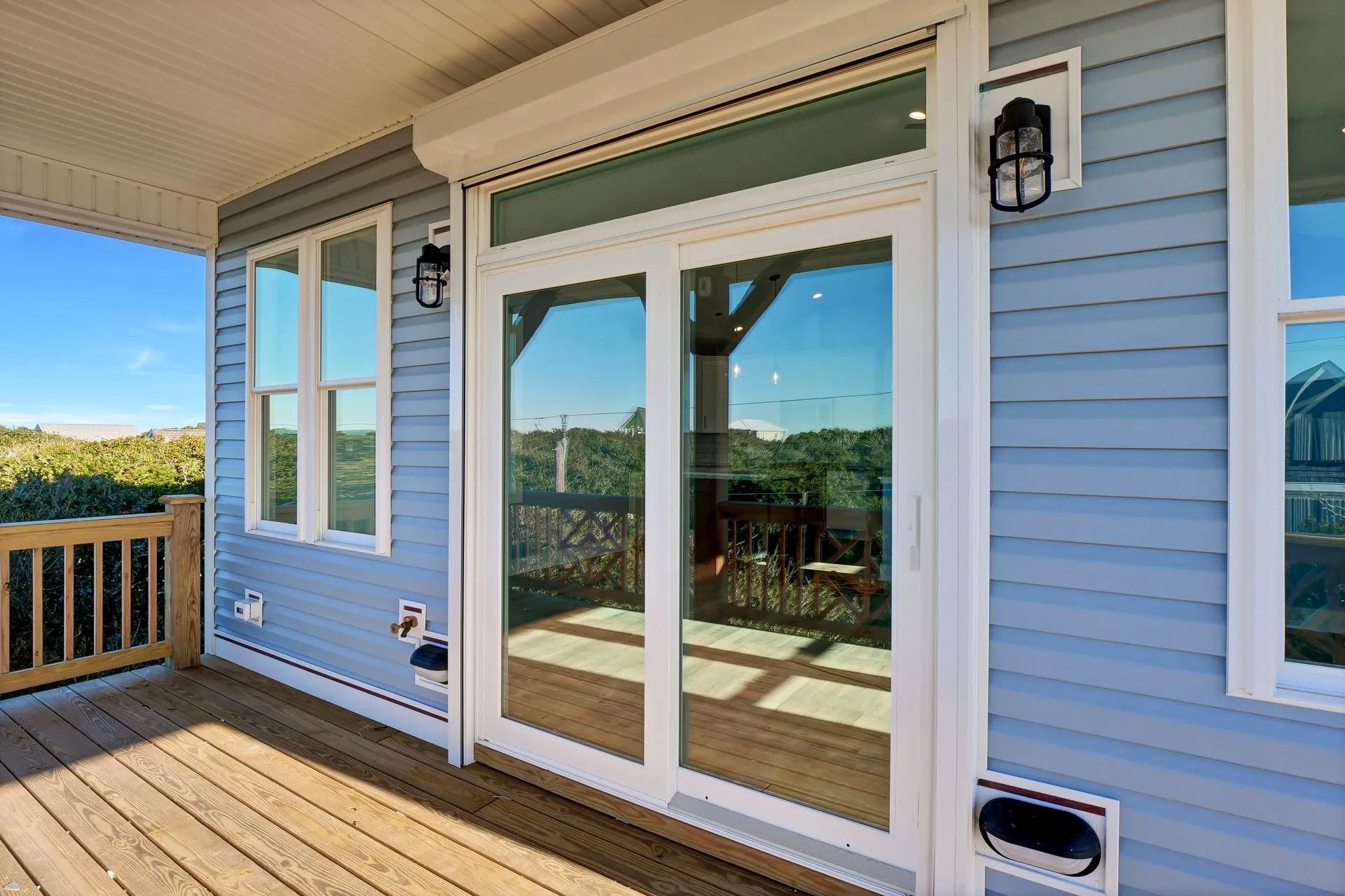 Blue house exterior with glass doors and a rolling shutter, leading to a wooden deck with a railing.