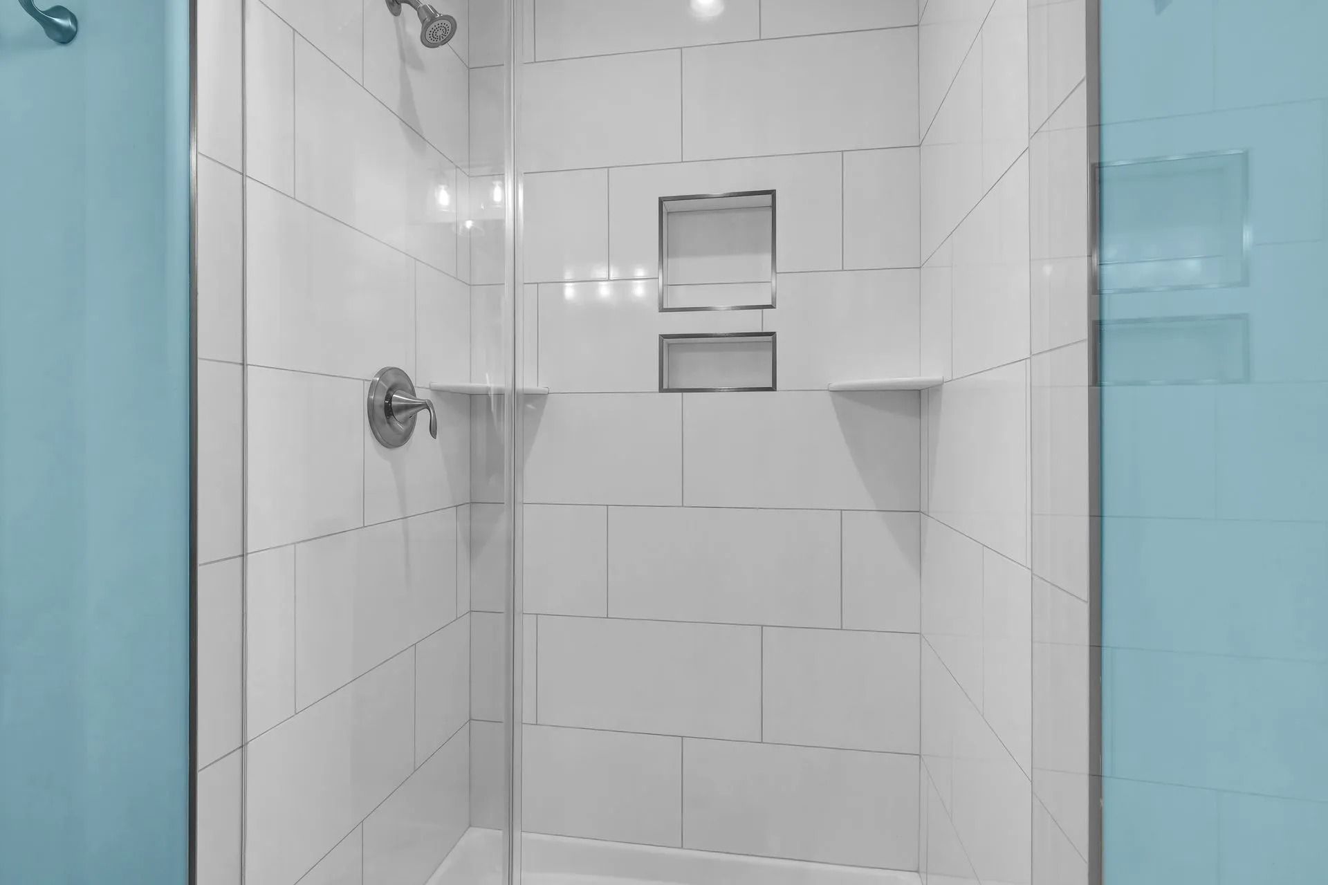 White tiled shower with built-in shelves and a shower head. The wall is light blue.