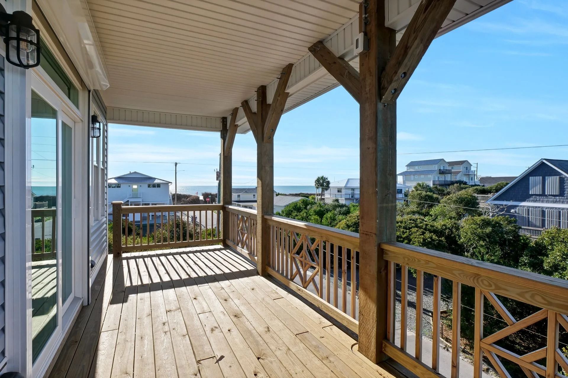 Wooden deck with ocean view, brown railings, support beams, and blue sky.