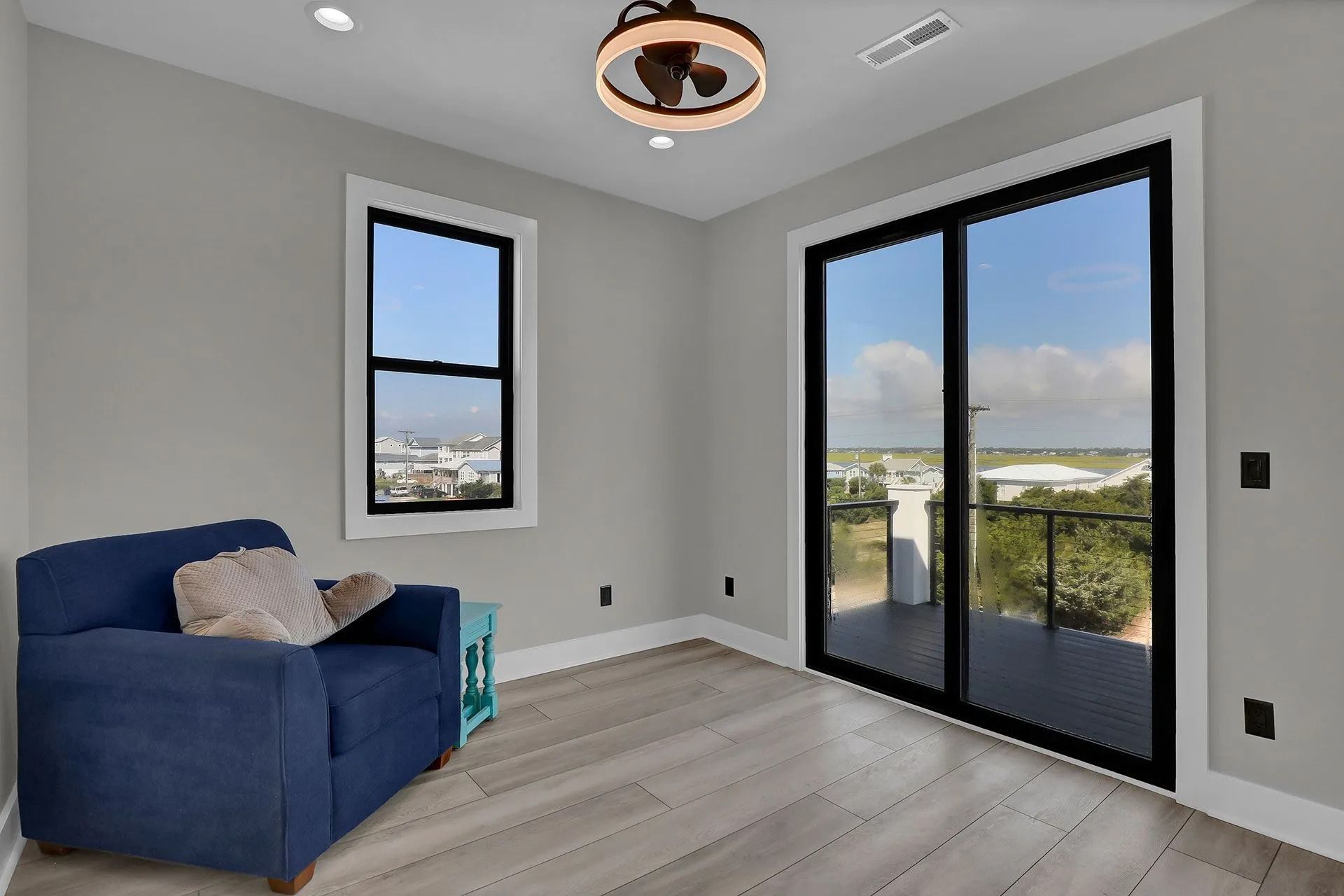 Blue armchair in a gray room, window and sliding glass door with a view of a deck and city.
