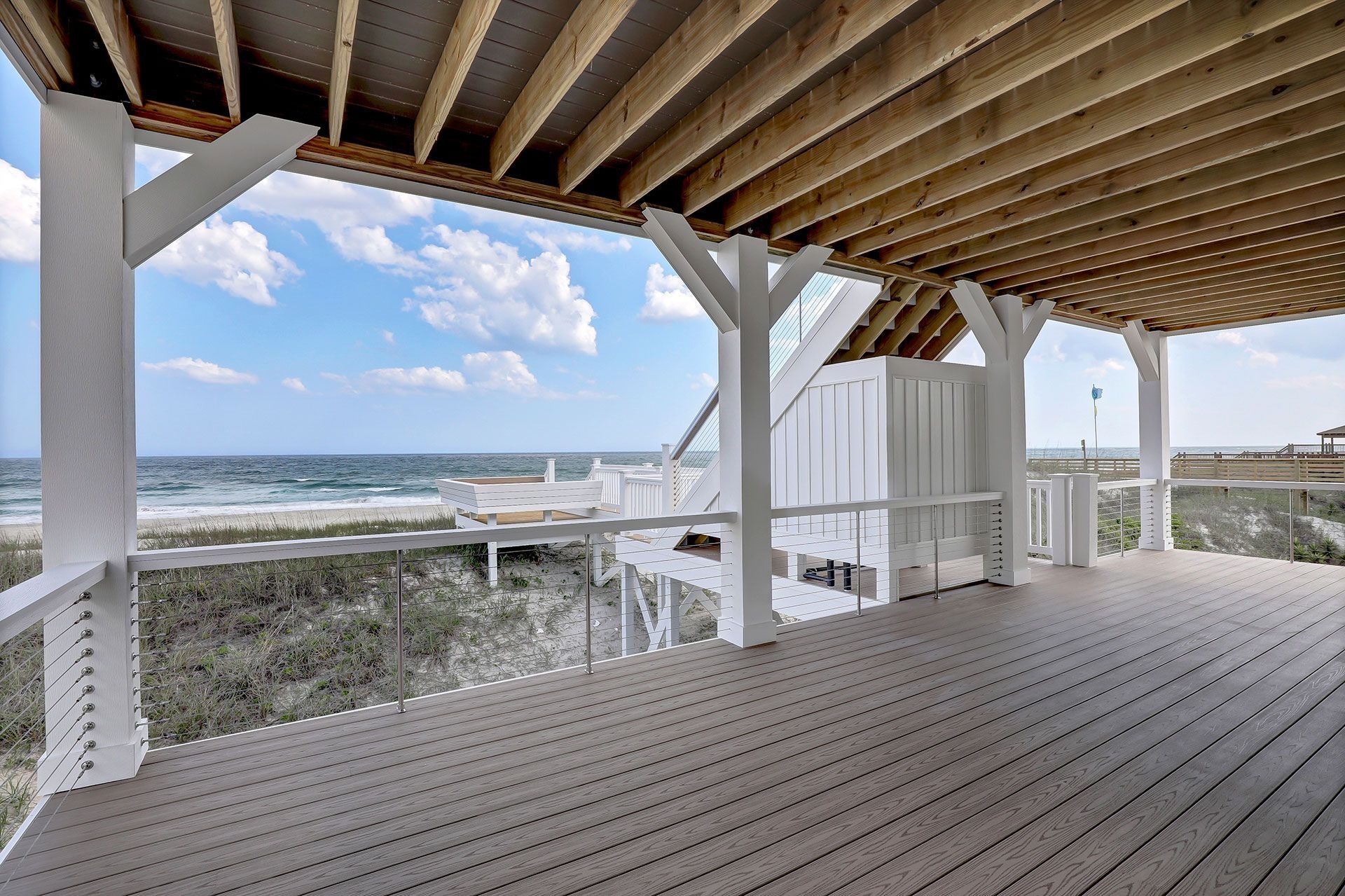 Deck overlooking ocean with white pillars, blue sky, and wooden ceiling.