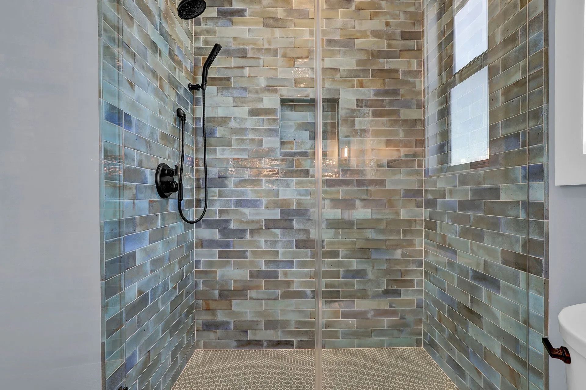 Shower with blue and grey brick-style tile, black fixtures, and a glass door.