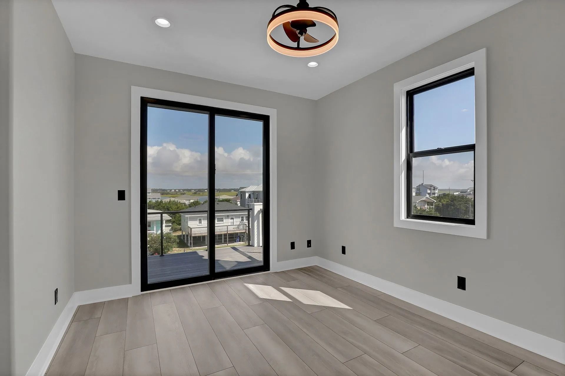 Empty room with gray walls, wood floors, and black-framed windows and sliding glass door.