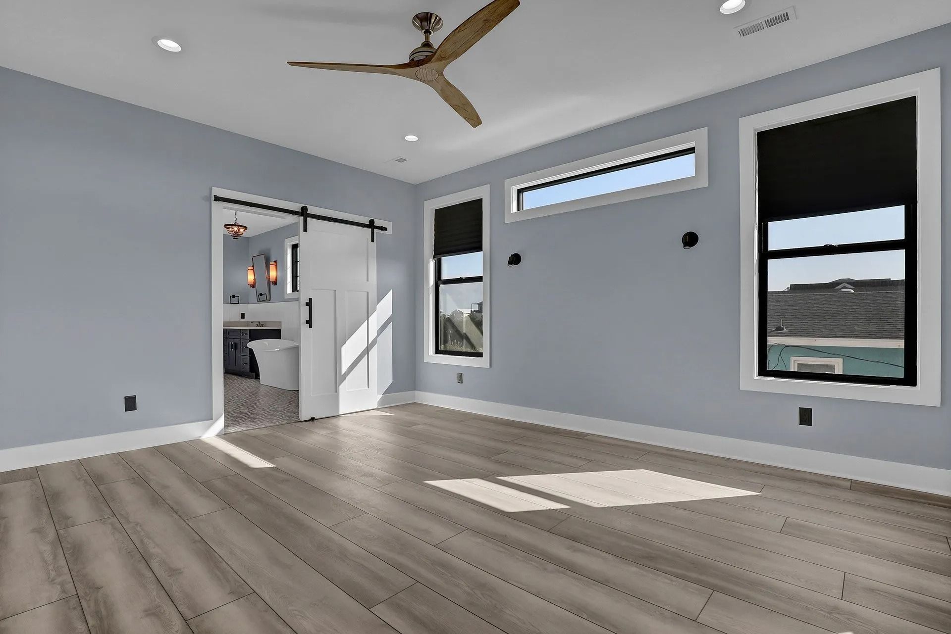 Empty bedroom with blue walls, wood-look flooring, and a sliding barn door leading to a bathroom.