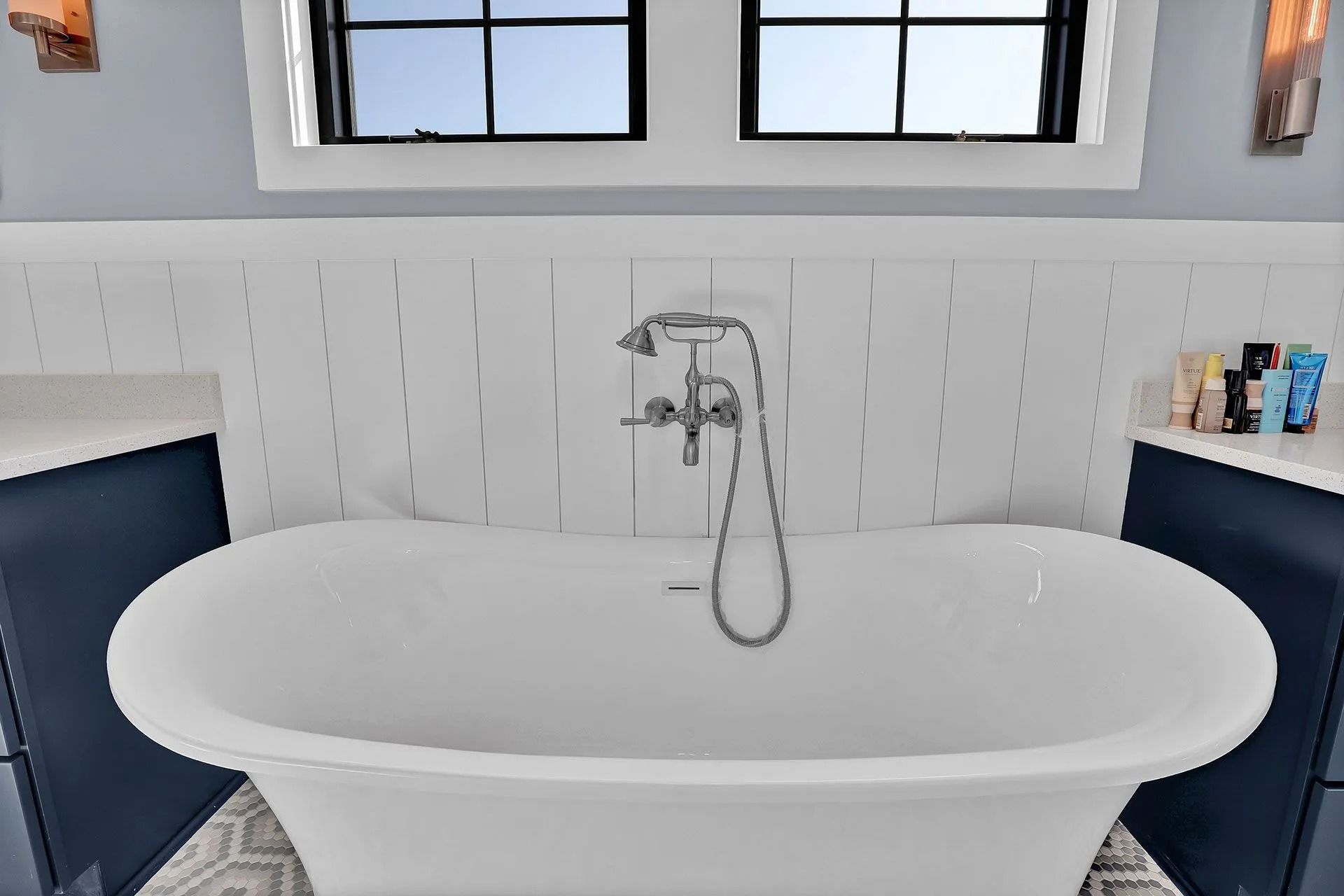 White freestanding bathtub in bathroom with blue cabinets and white tile wall.