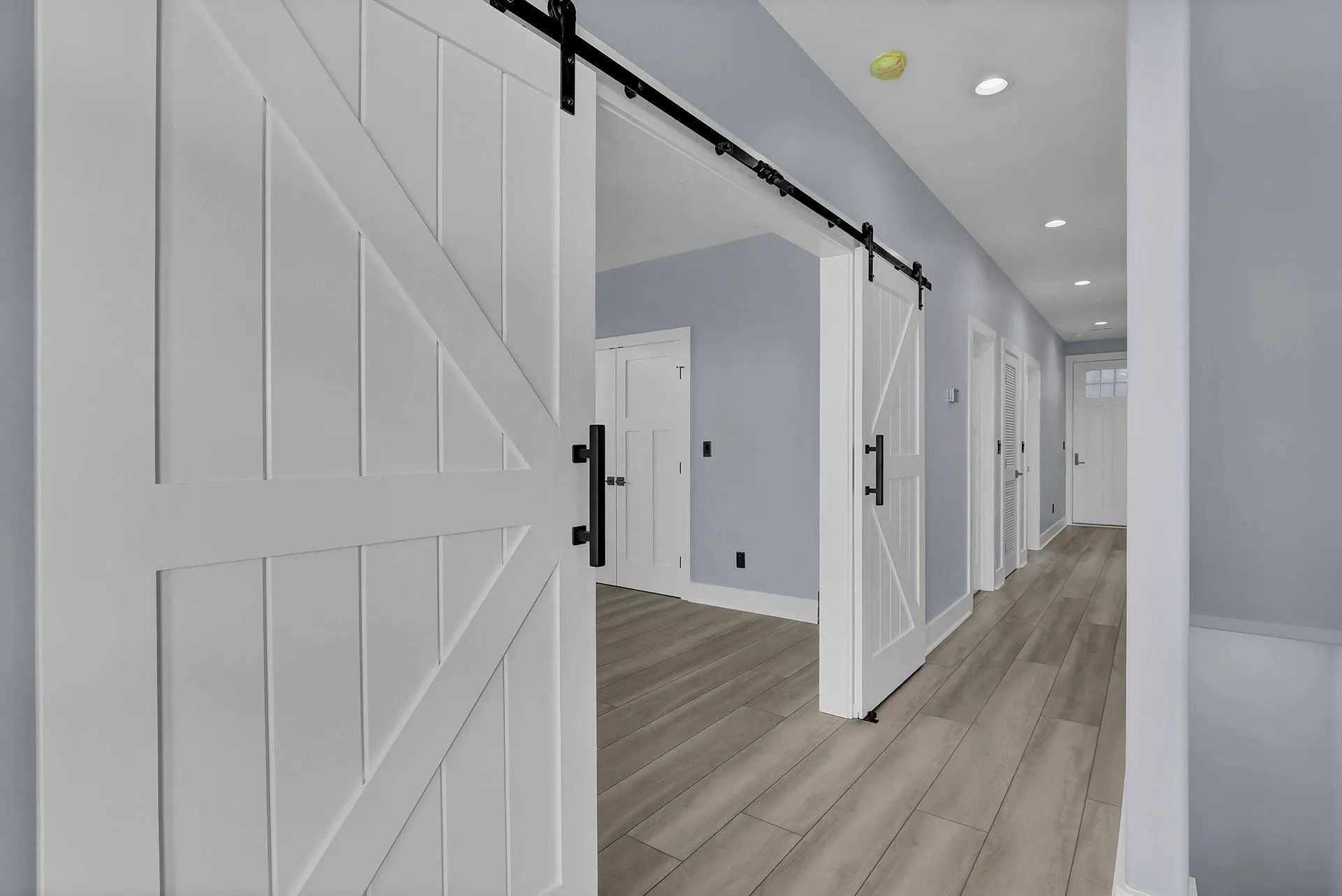 Hallway with white barn doors, light wood-look floors, and gray walls.