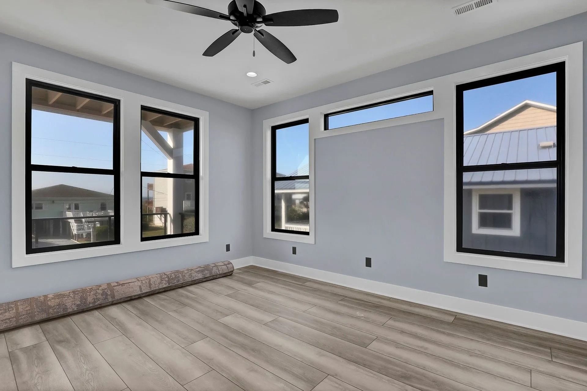 Empty bedroom with light blue walls, wood-look floor, windows, and ceiling fan.