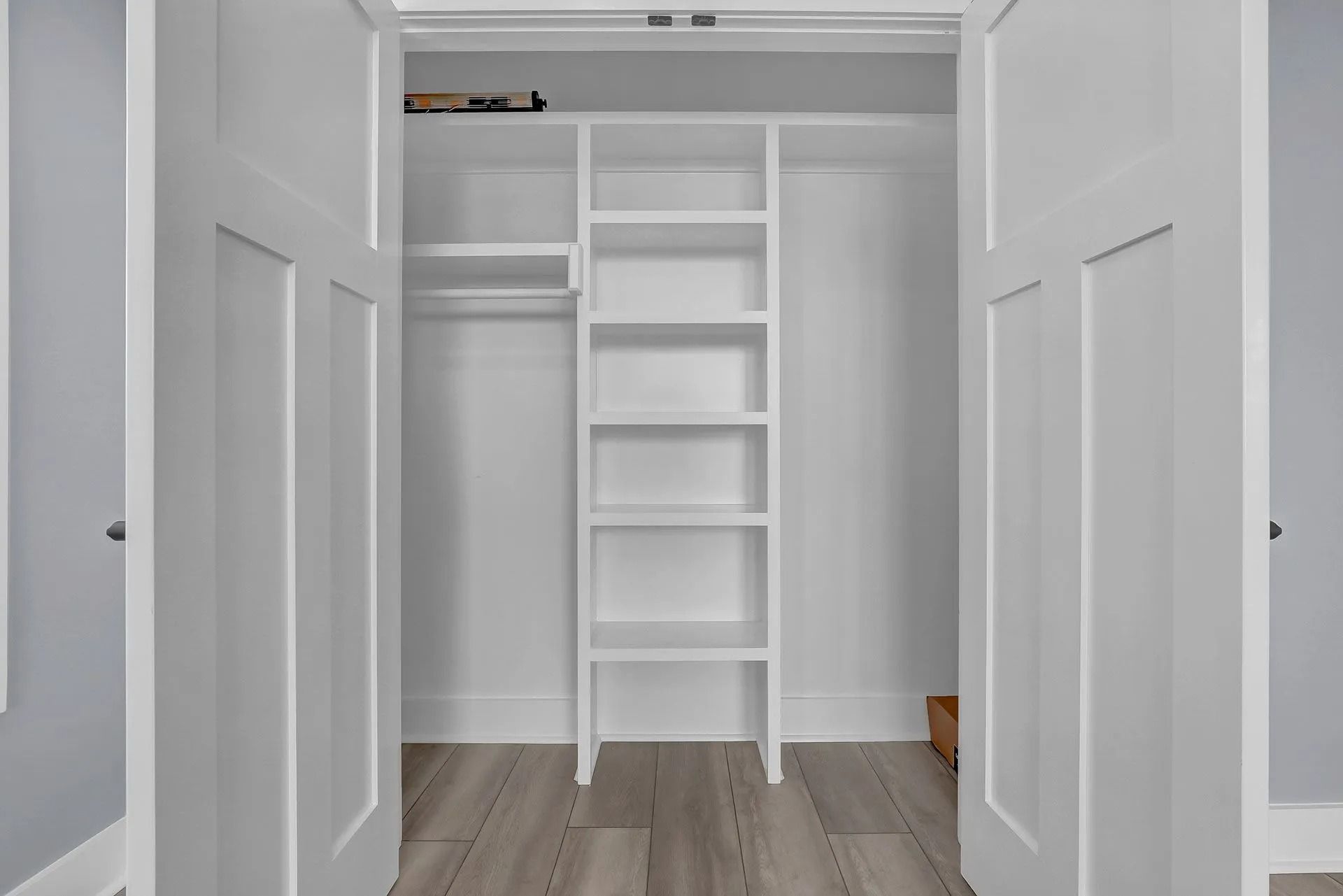 White closet interior with shelves, rod, and open doors. Light gray flooring.