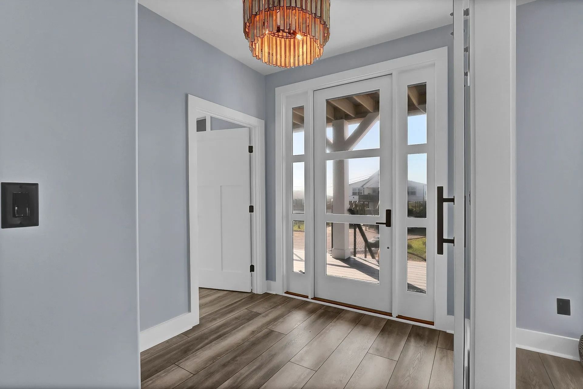 Interior doorway with glass panels, white trim, and a chandelier; light blue walls and wood flooring.