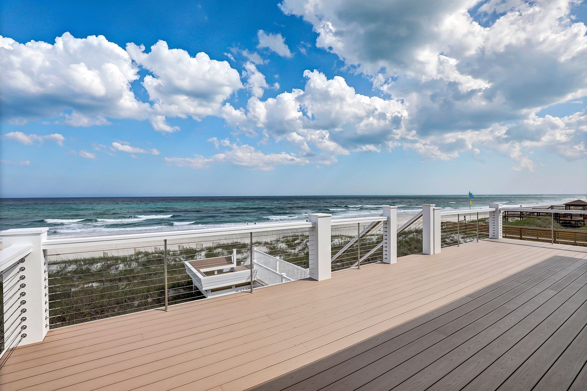 Wooden deck overlooking the ocean with a white railing. Blue sky with clouds.