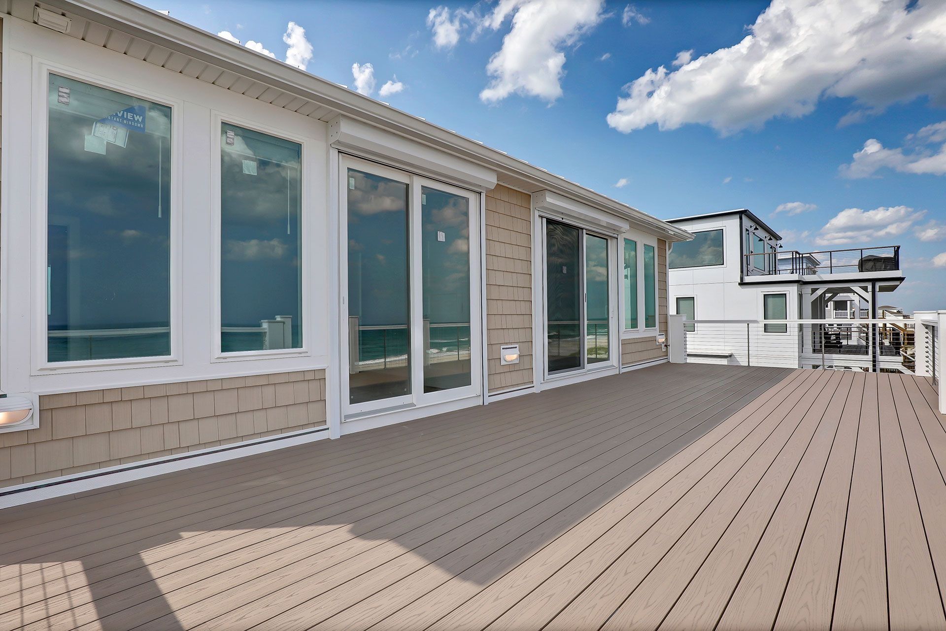 Deck with ocean view; windows along siding. Blue sky, white clouds.