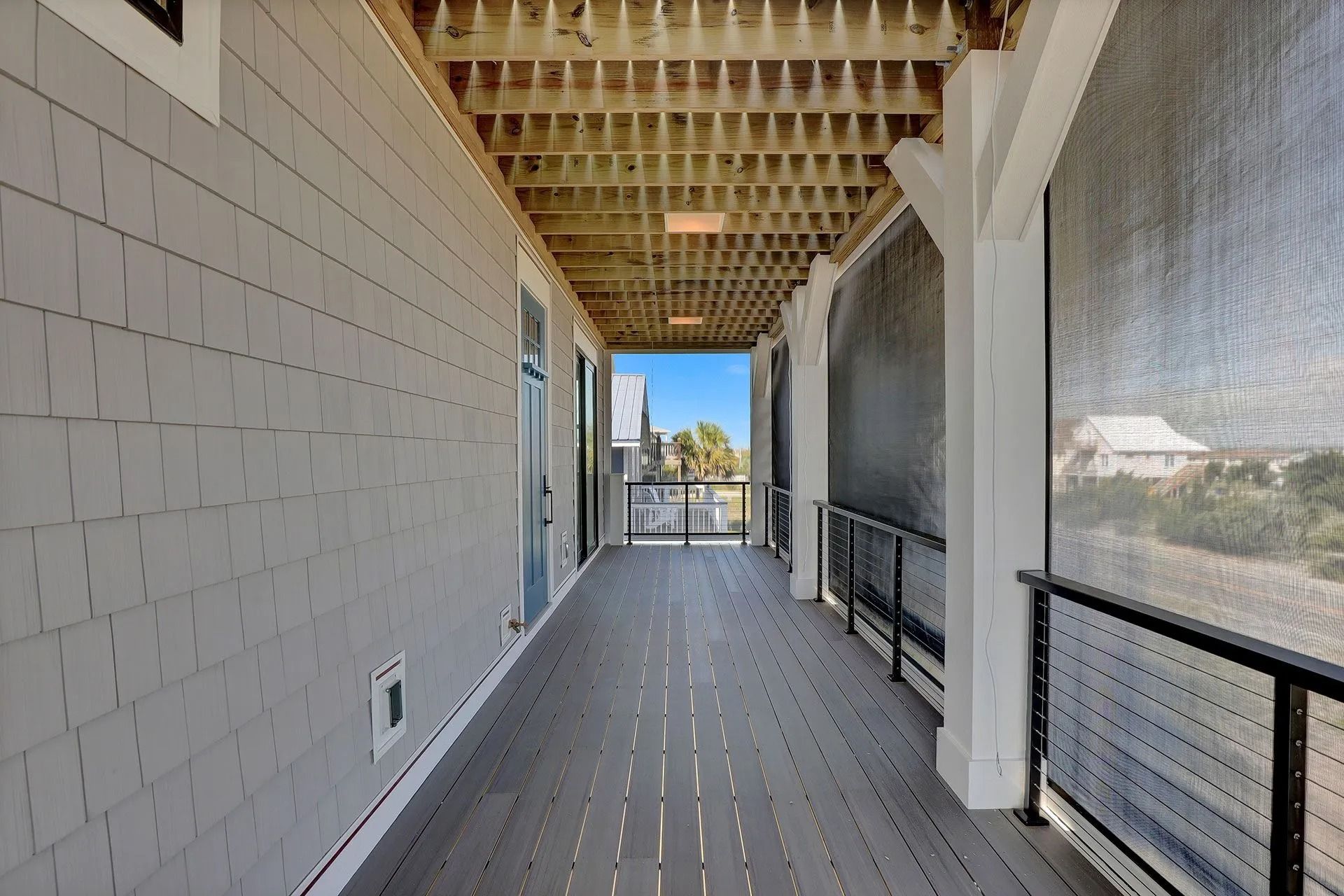Covered outdoor walkway with gray siding, wooden deck, and metal railings overlooking a view.