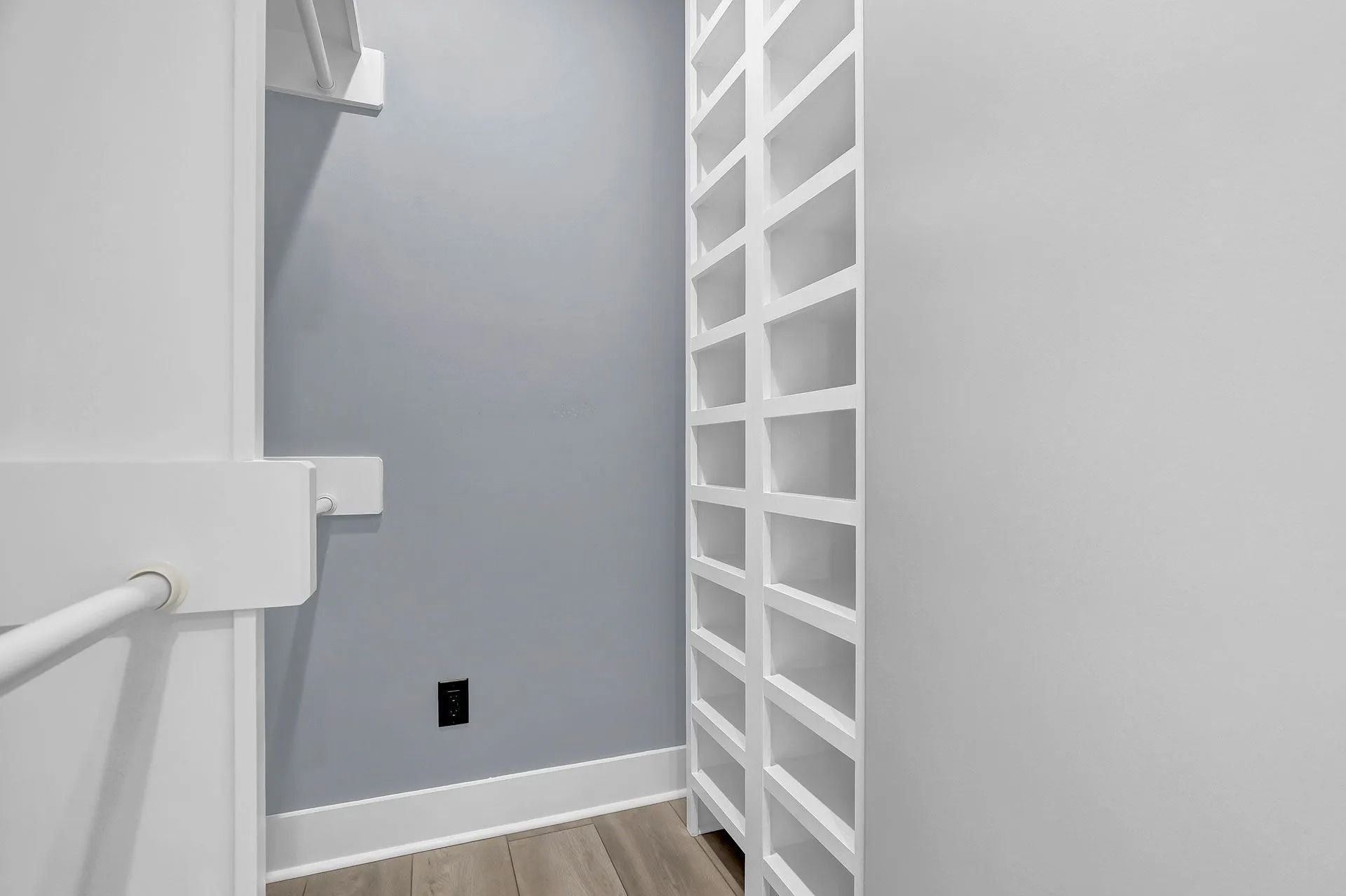 White closet with shelves and rods, gray wall, wood-look floor, and a black outlet.