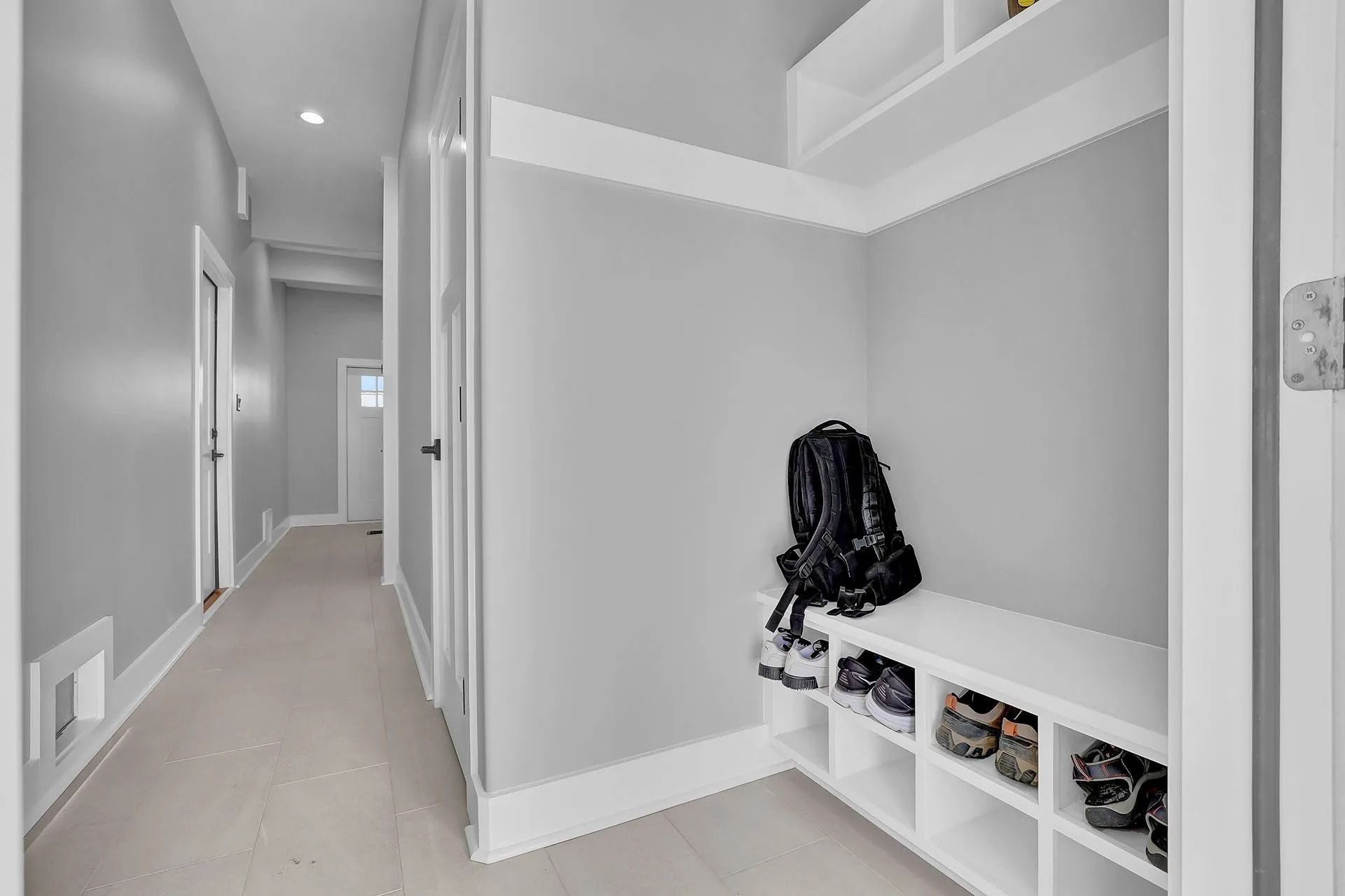 Hallway with gray walls and a white-shelved entryway bench holding shoes and a backpack.