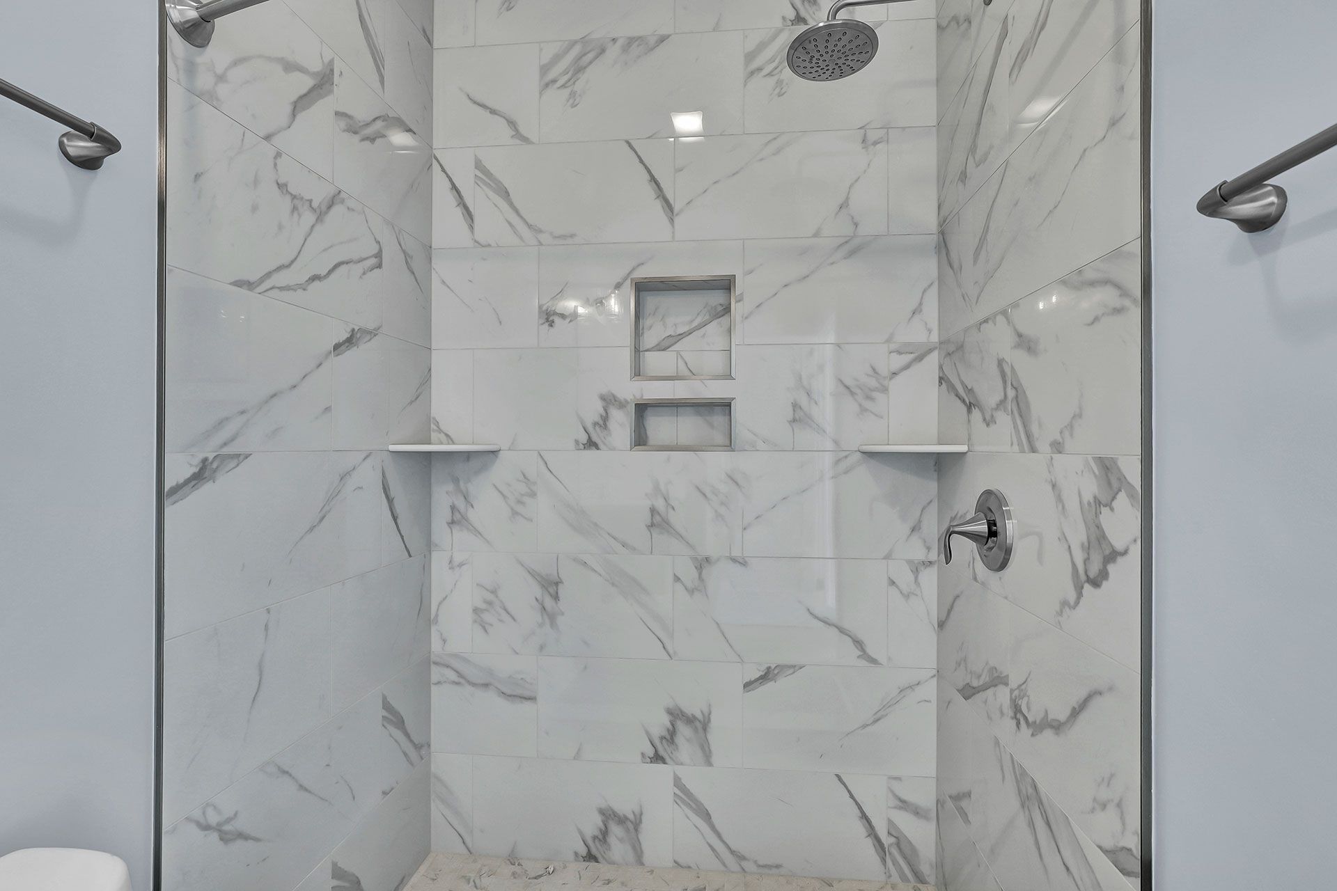 Shower with marble-patterned tile and glass doors, featuring two built-in shelves and two recessed niches.