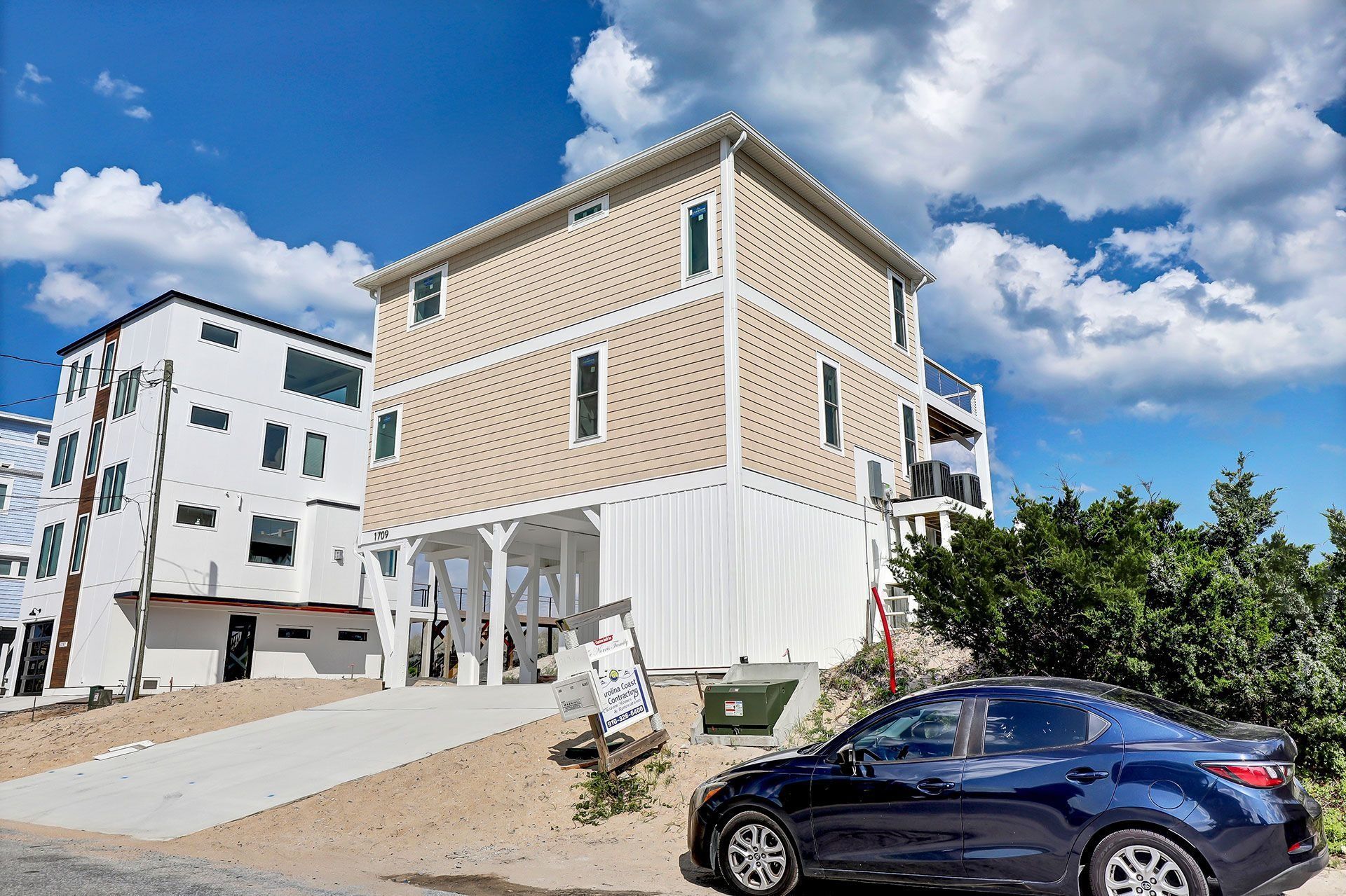 Beach house with beige siding, blue sky, and a blue car parked in front.