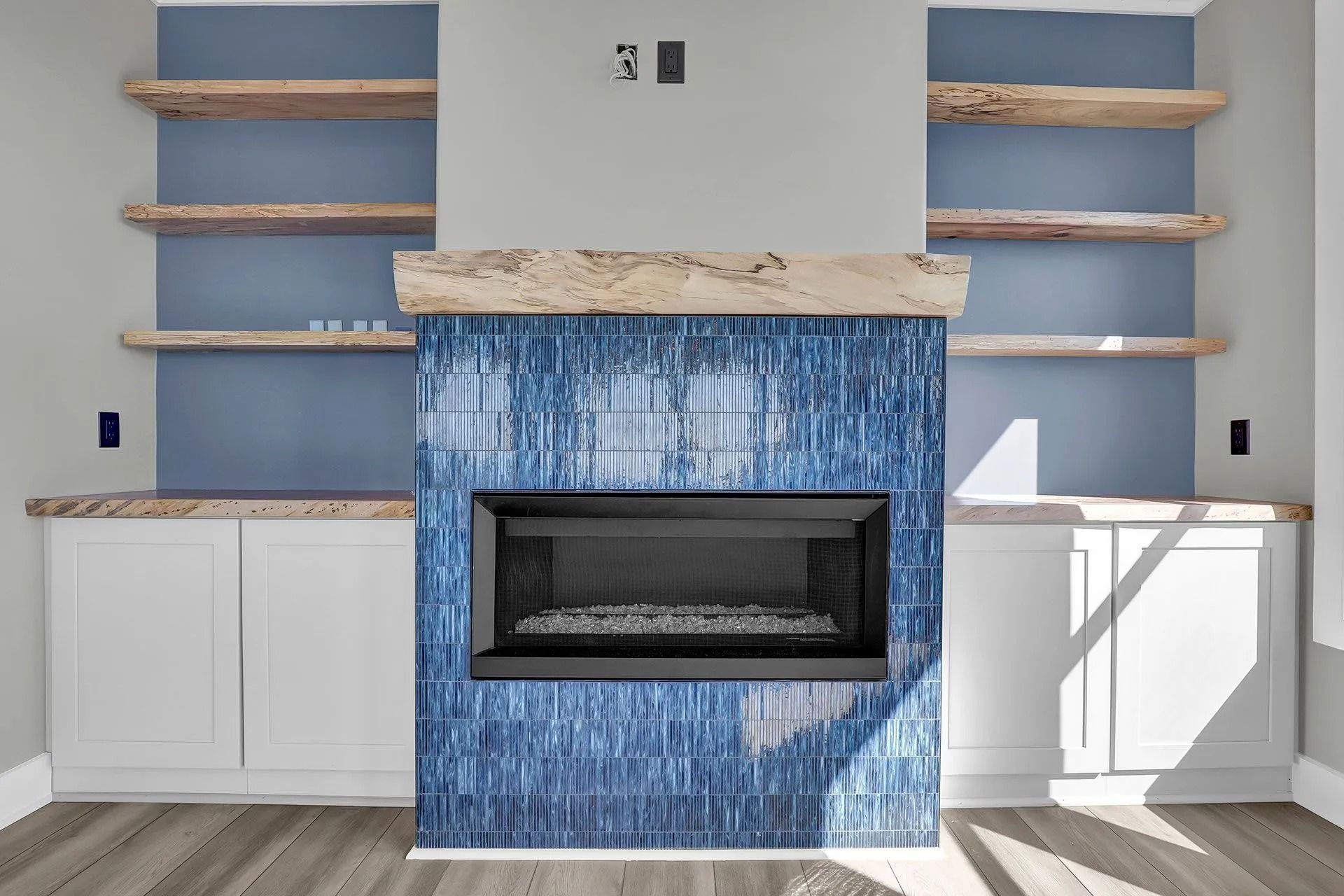 Fireplace with blue tiled surround, white cabinets, and wooden shelves against a blue wall.