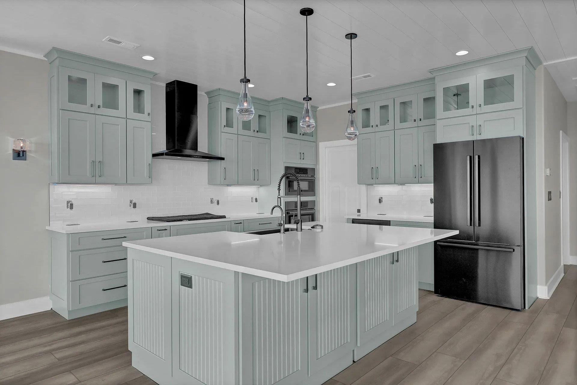 Light blue kitchen with island, stainless steel appliances, and overhead pendant lights.