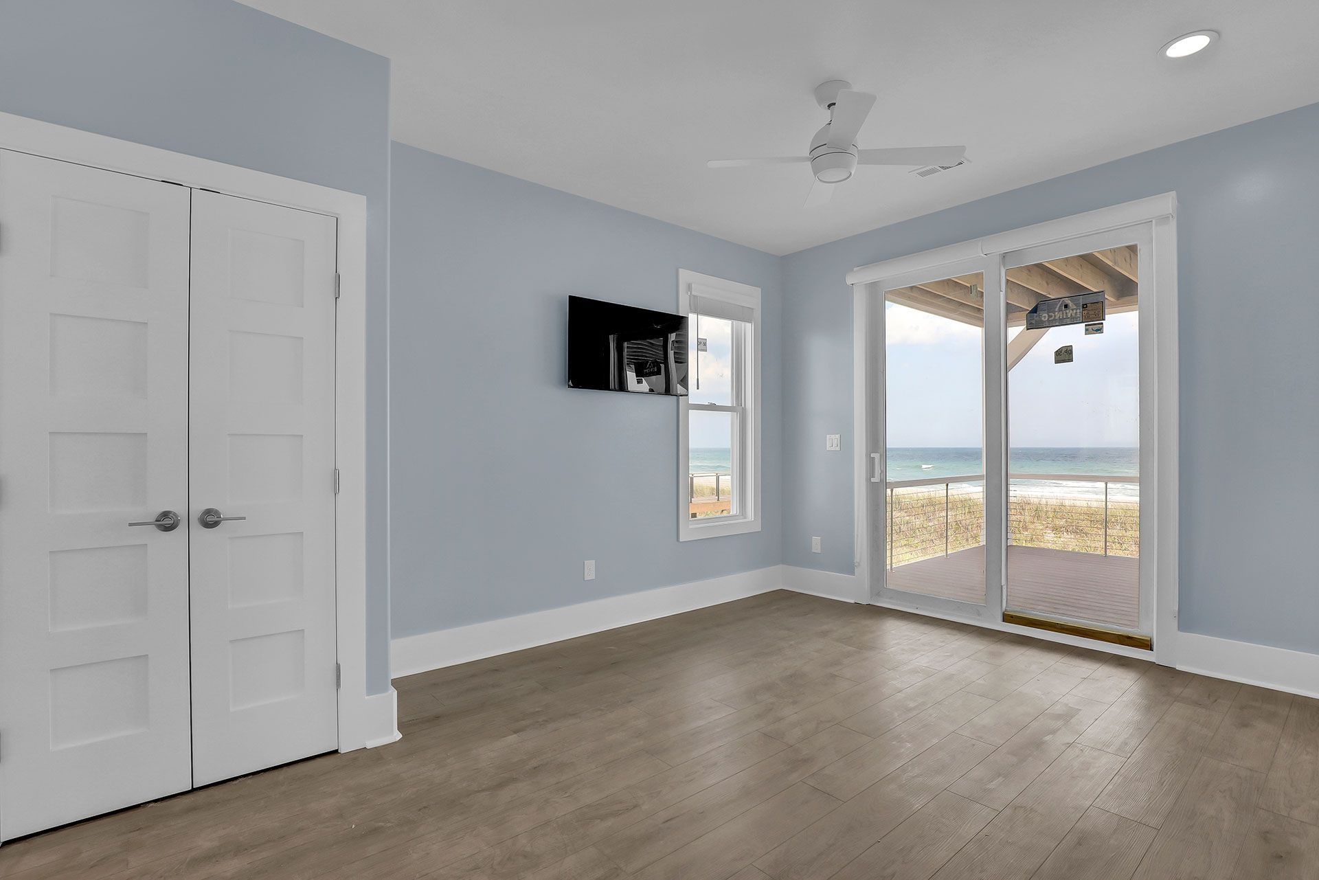 Empty blue bedroom with beach view, sliding glass doors, and hardwood floors.