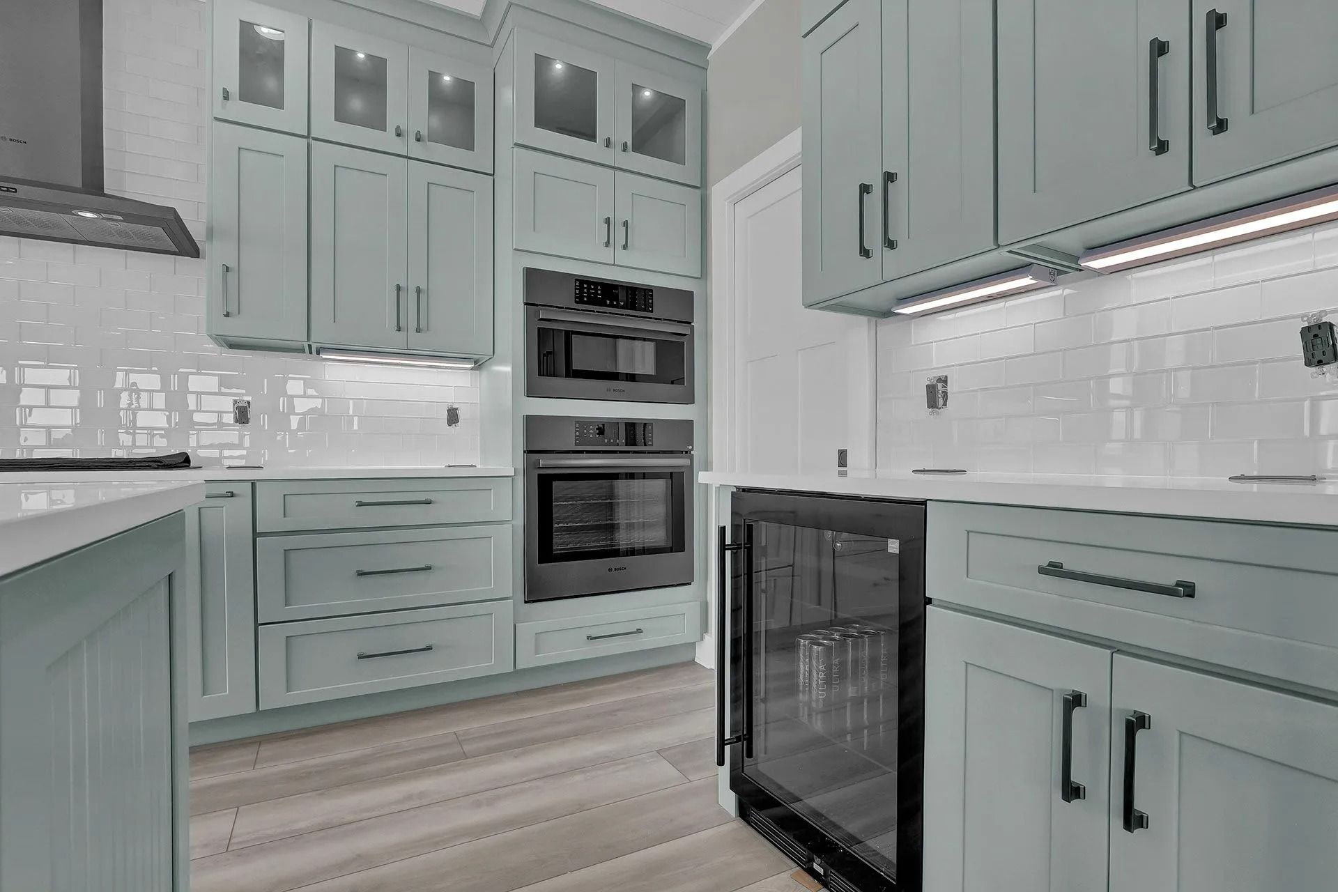 A modern kitchen with light blue cabinets, white backsplash, and black appliances.