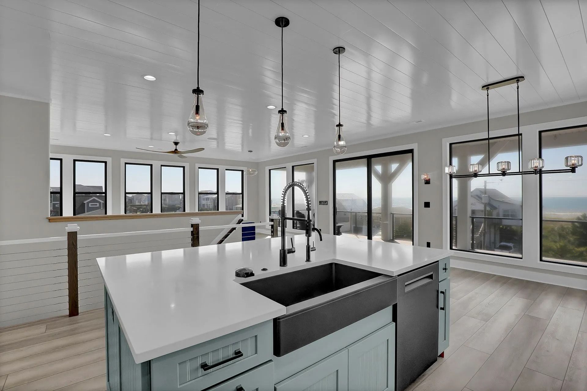 Modern kitchen with blue island, stainless steel sink, large windows, and pendant lights.