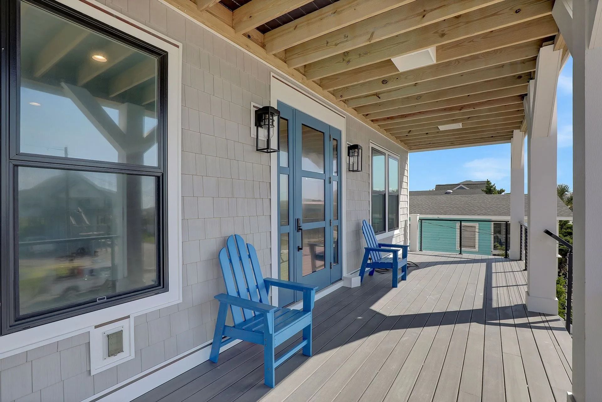 Covered porch with blue chairs, blue door, and gray siding.