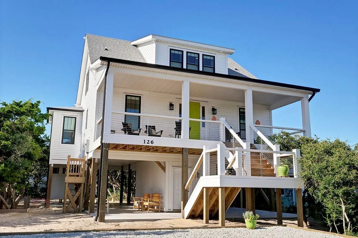 White beach house on stilts with green door and porch.