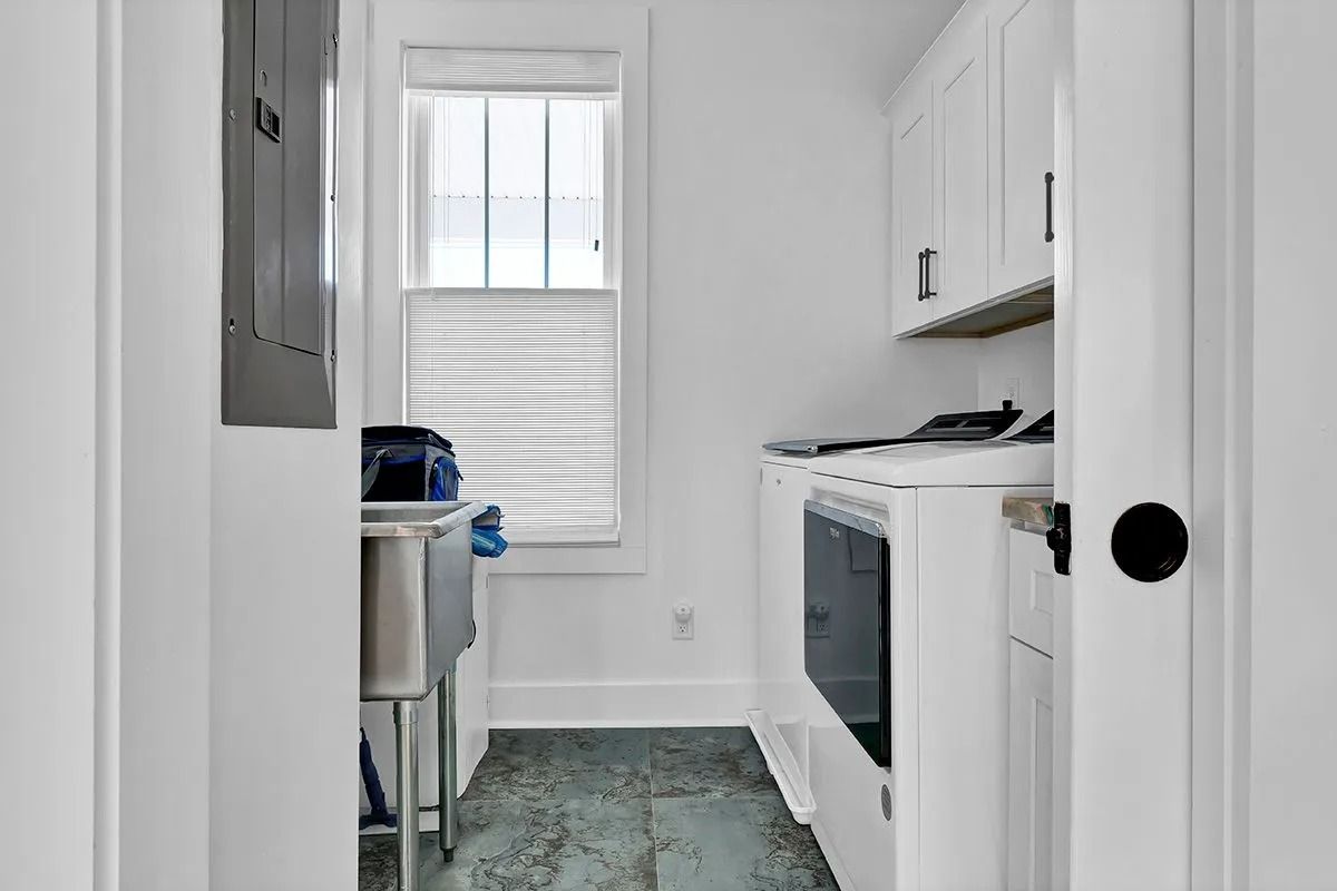 Laundry room with white cabinets, washing machine, and a window with blinds.