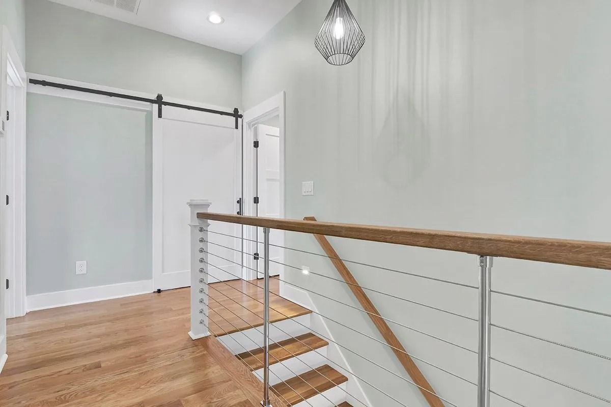 Hallway with stairs and light wood floors, a barn door, and a modern cable railing.