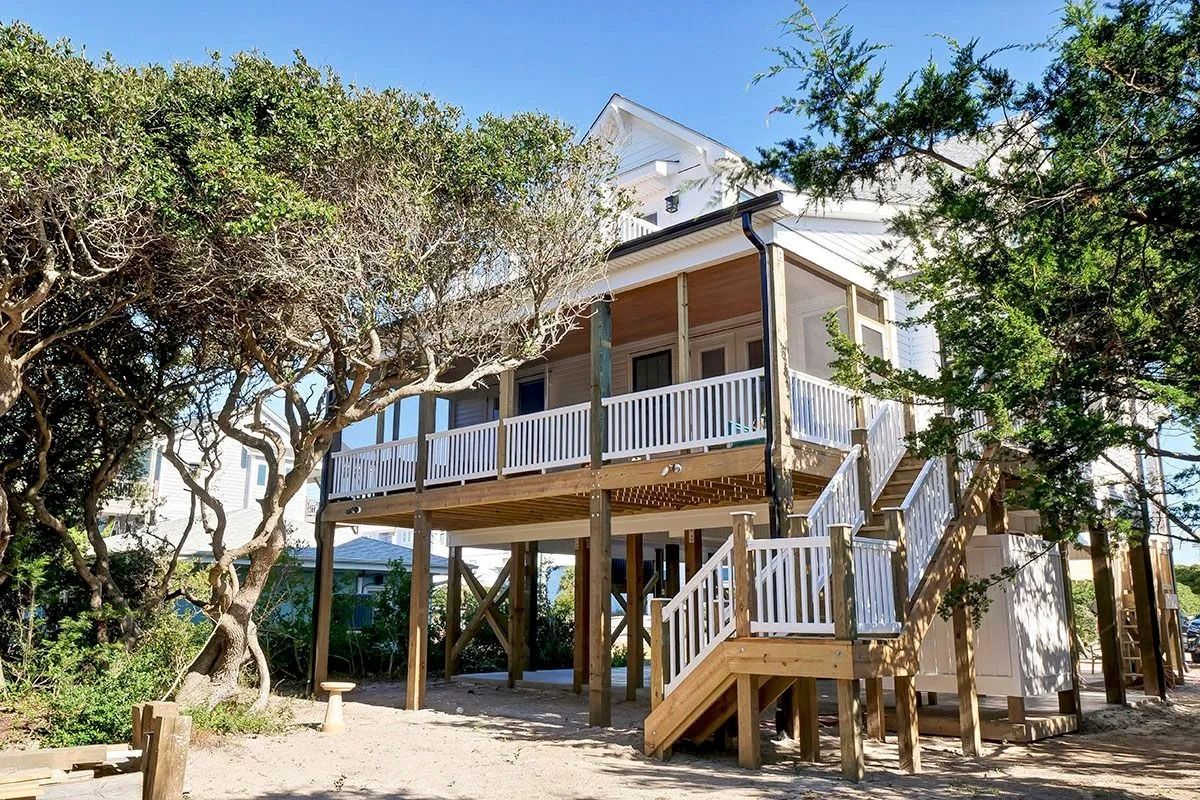 Coastal home with a deck and stairs surrounded by trees.