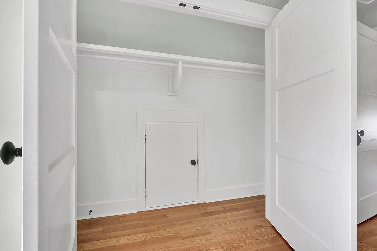Empty white closet with open doors, wooden floor, and a small door.