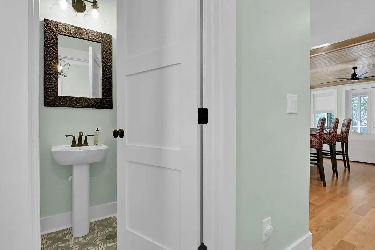 Doorway view into a powder room with a pedestal sink, and a dining room with wooden floor.