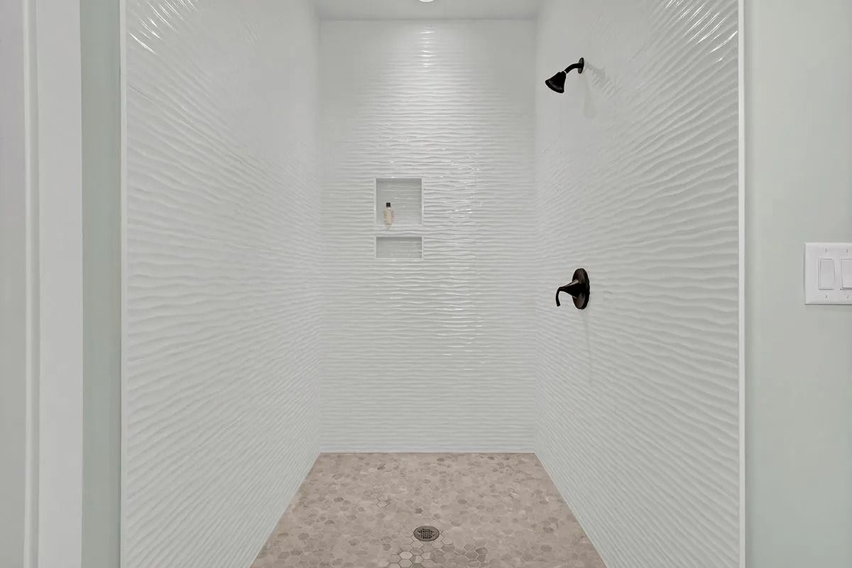 White-tiled shower with black fixtures; stone floor, centered drain.
