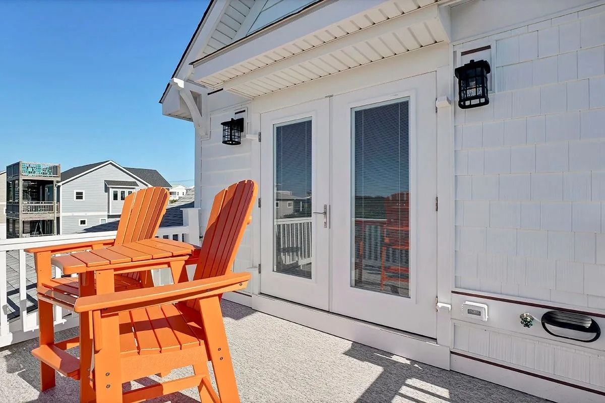 Orange Adirondack chairs on a deck, with French doors and ocean view. Bright blue sky.