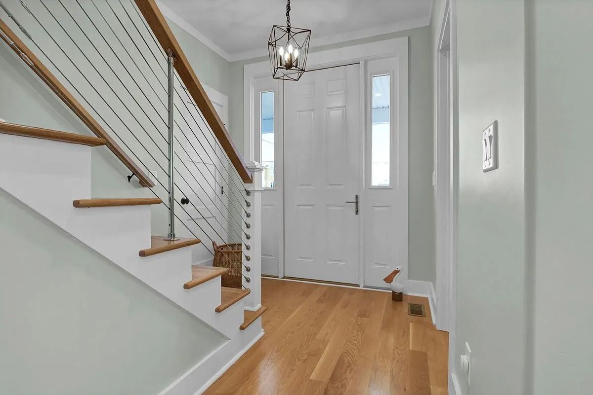 Staircase with wooden steps and cable railing, leading to a front door with sidelights. Hardwood floor.