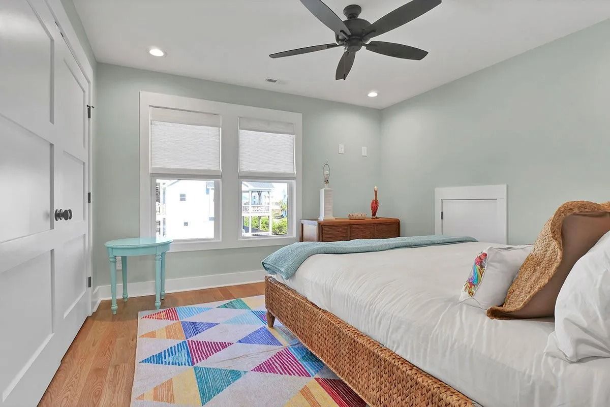 Bedroom with light blue walls, wooden floors, and a bed with a colorful rug.