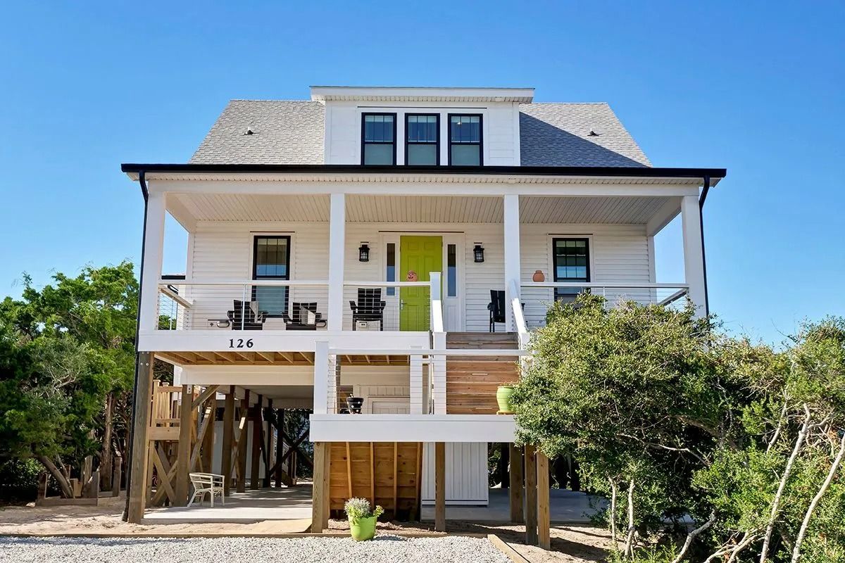 White beach house on stilts with a green door and wrap-around porch.