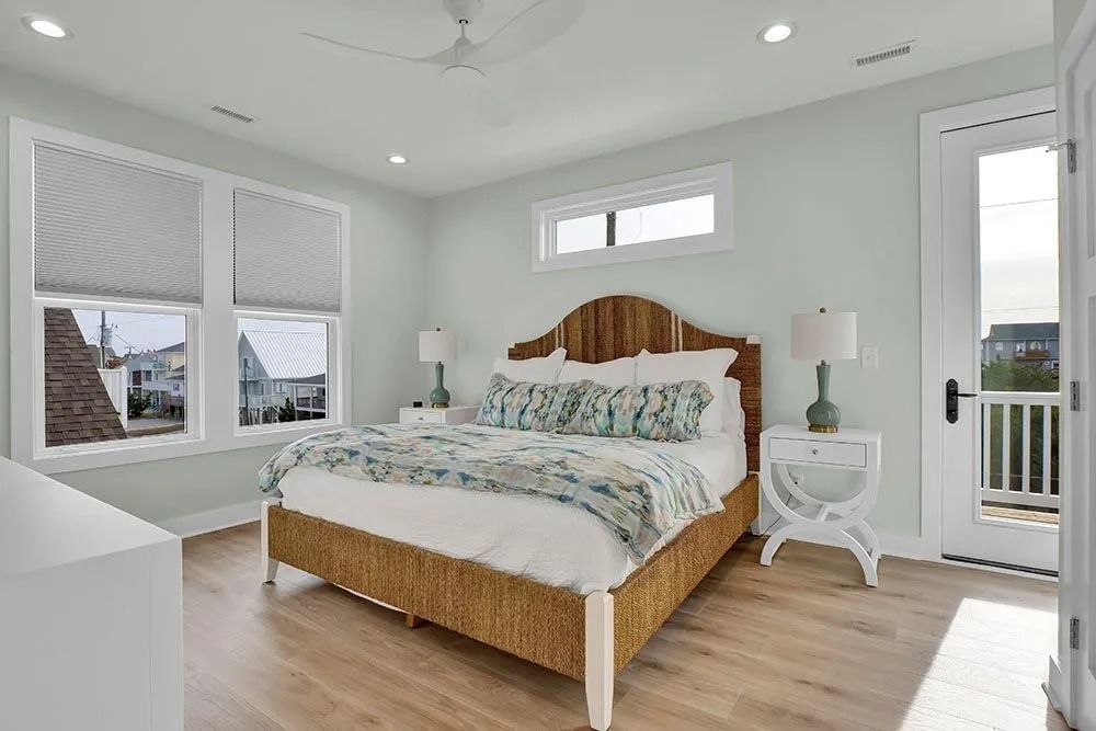 Bedroom with light blue walls, wicker bed, and large windows with white shades.