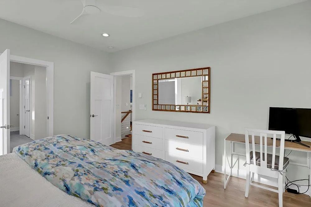 Bedroom with white walls, bed with floral bedding, dresser, desk, and mirror.