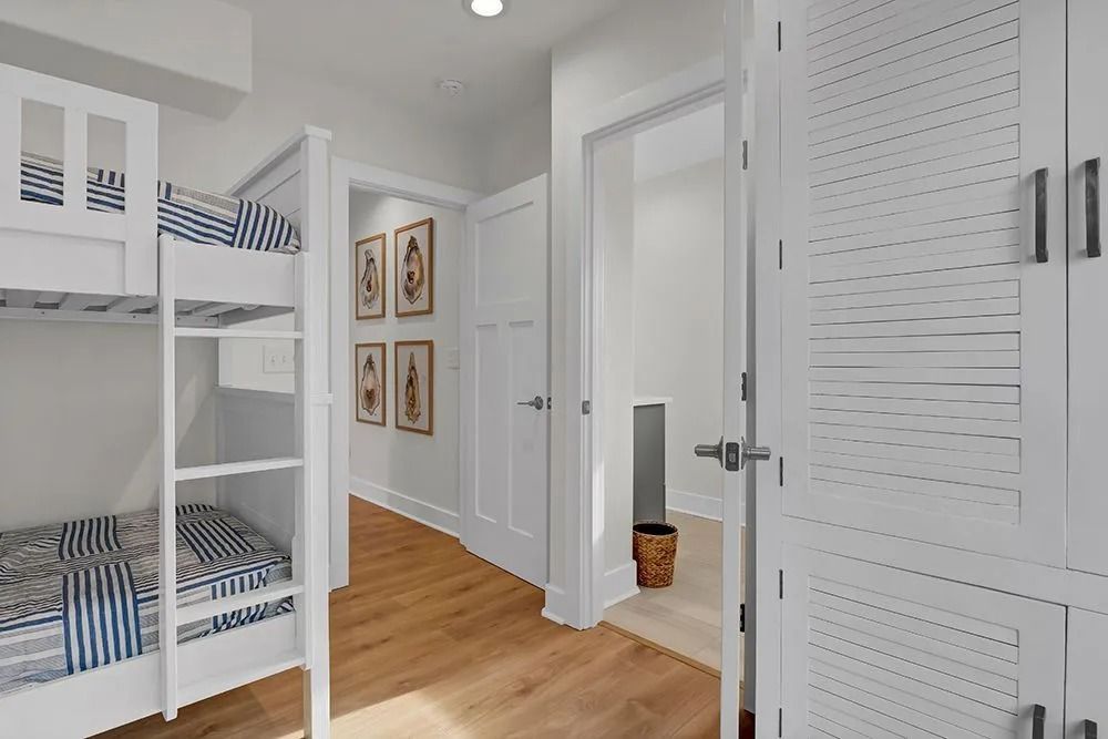 Bedroom hallway with bunk beds, white cabinets, artwork, and wood flooring.