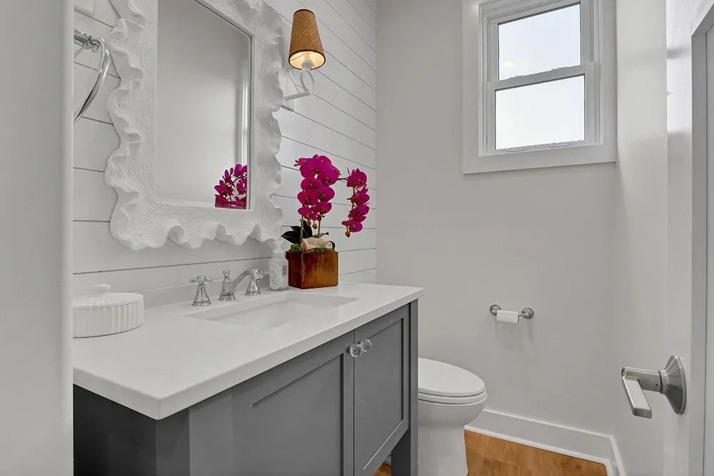 Bathroom with gray vanity, white countertop, ornate mirror, and orchid.